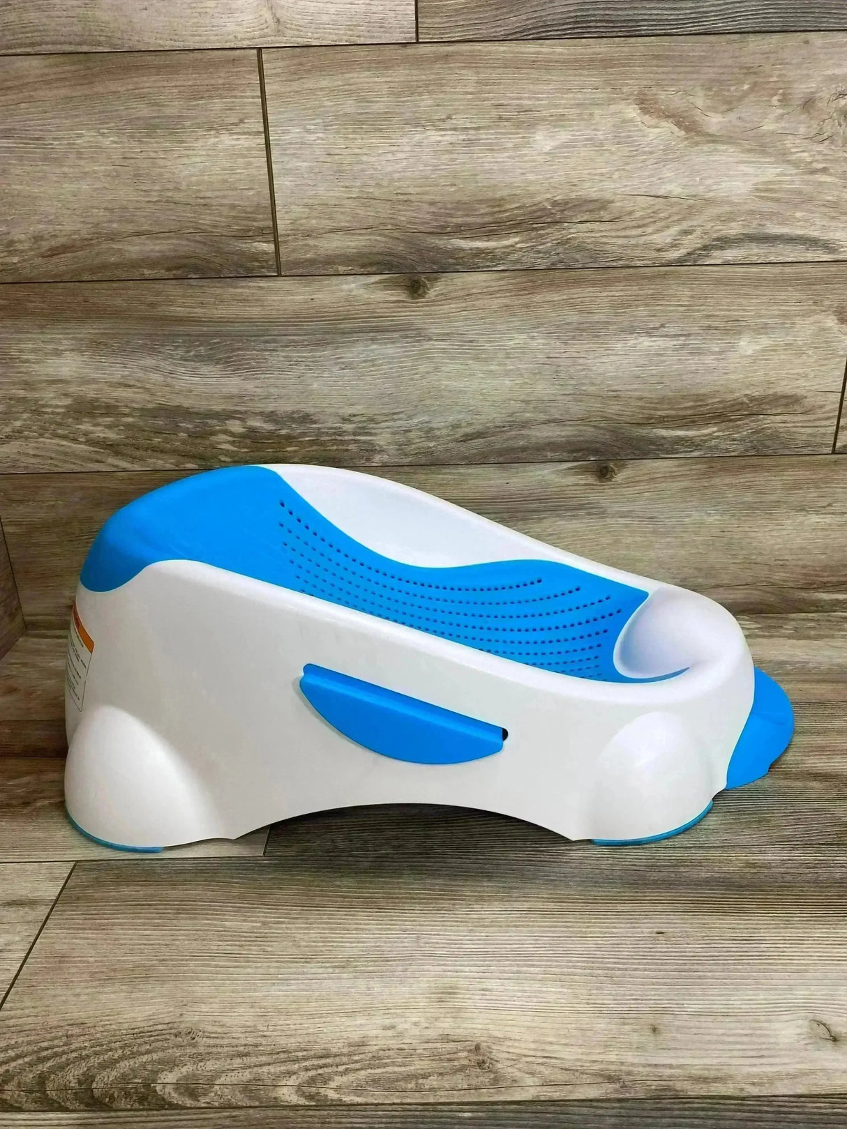 Side view of Munchkin Clean Cradle baby bathtub showing blue non-slip insert and contoured head support on wood floor