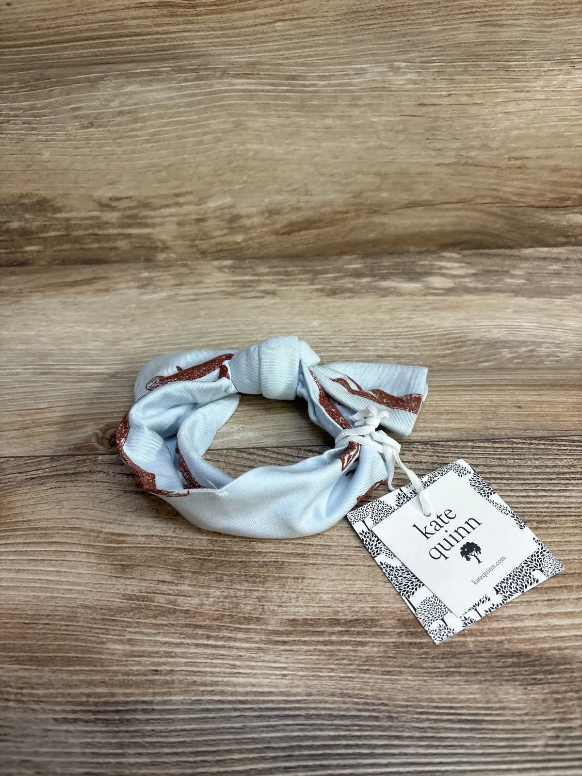Top view of Kate Quinn baby bow headband size 0-6 months showing knotted bow and rust fox print on light blue fabric