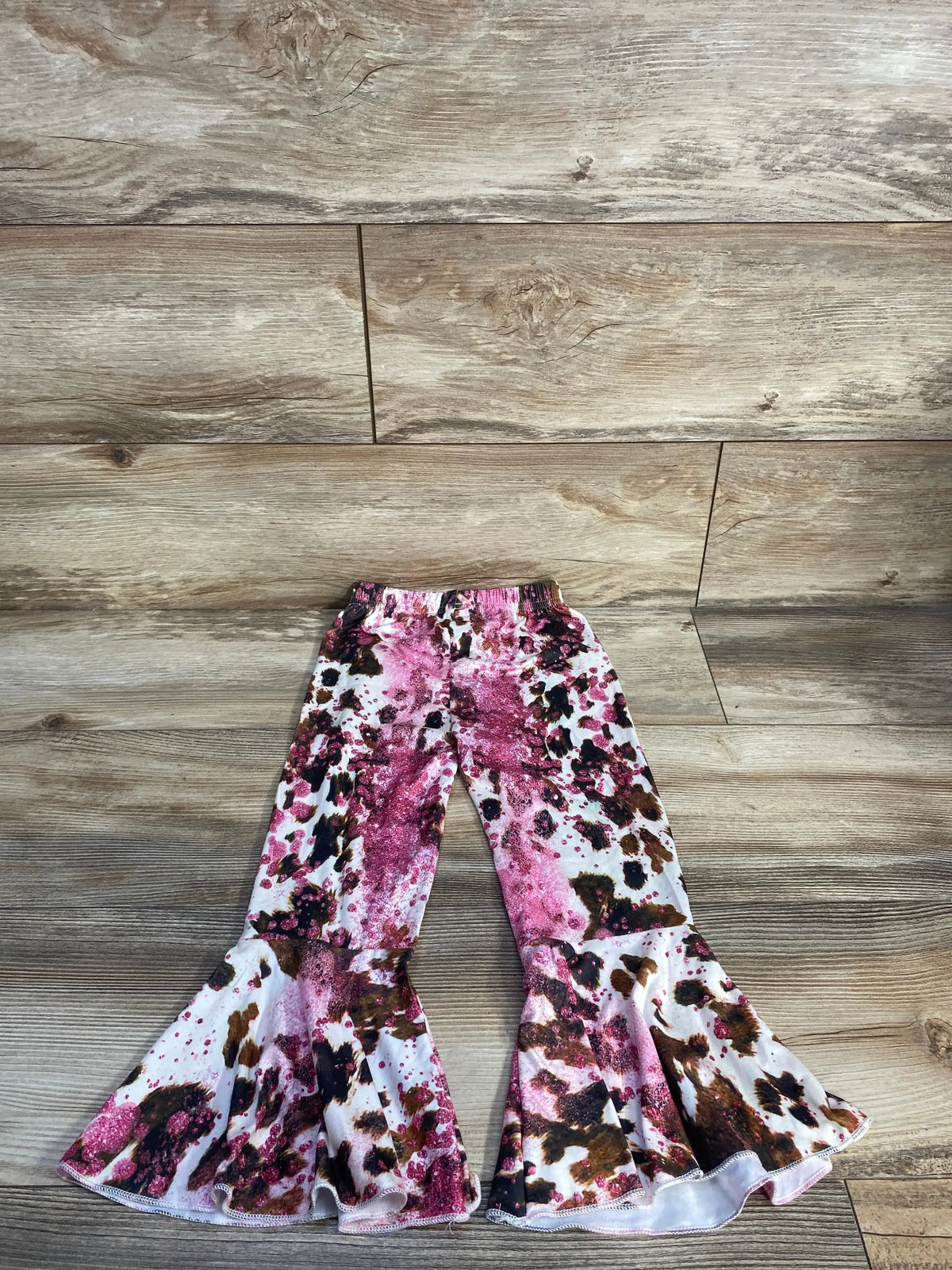 Front view of toddler flared pants showcasing a pink floral pattern and elastic waistband on a wood floor