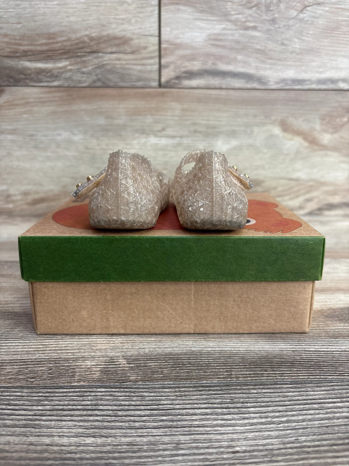 Rear view of sparkly toddler jelly shoes with ankle straps on a cardboard shoe box
