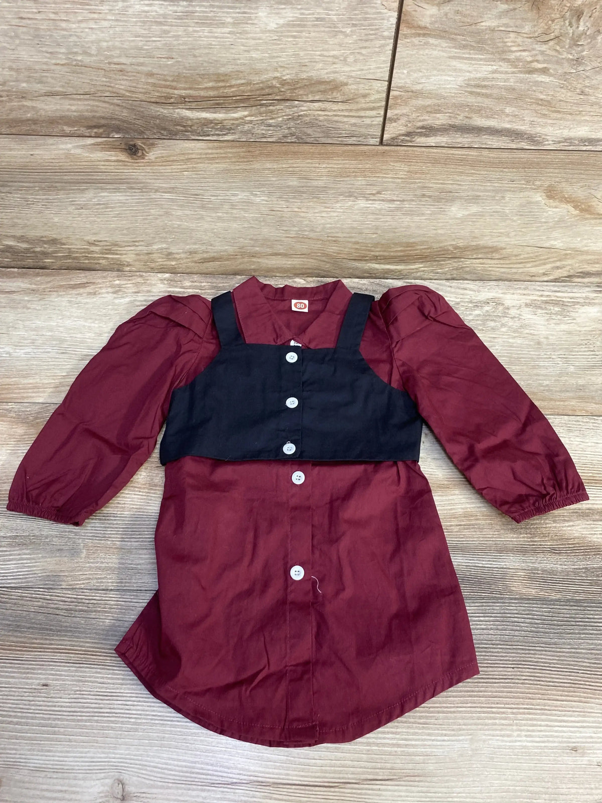 Maroon button-up dress with puff sleeves and attached black cropped vest on wood floor