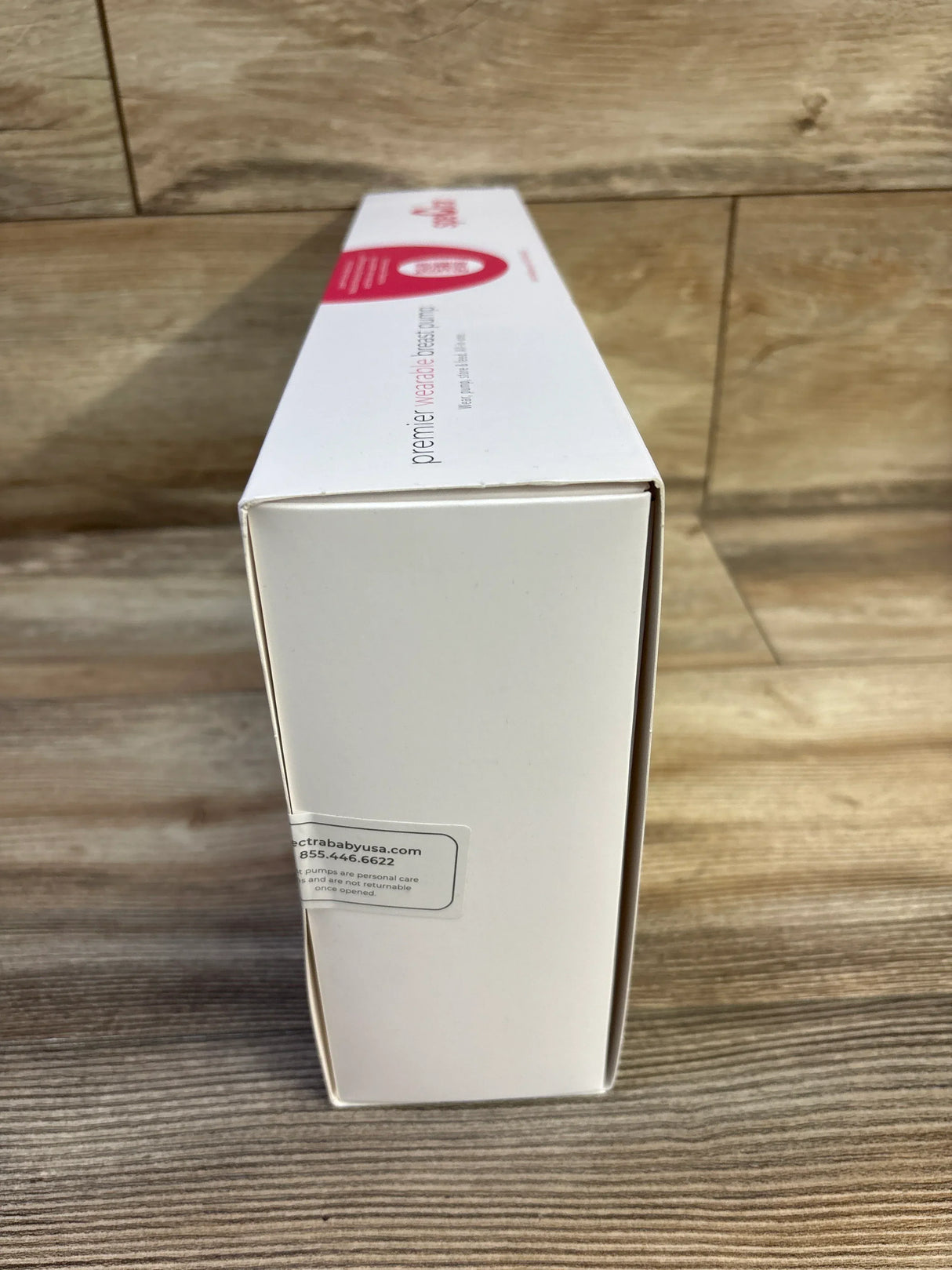 End view of Spectra Premier wearable electric breast pump box showing sealed white packaging with manufacturer sticker on wood surface