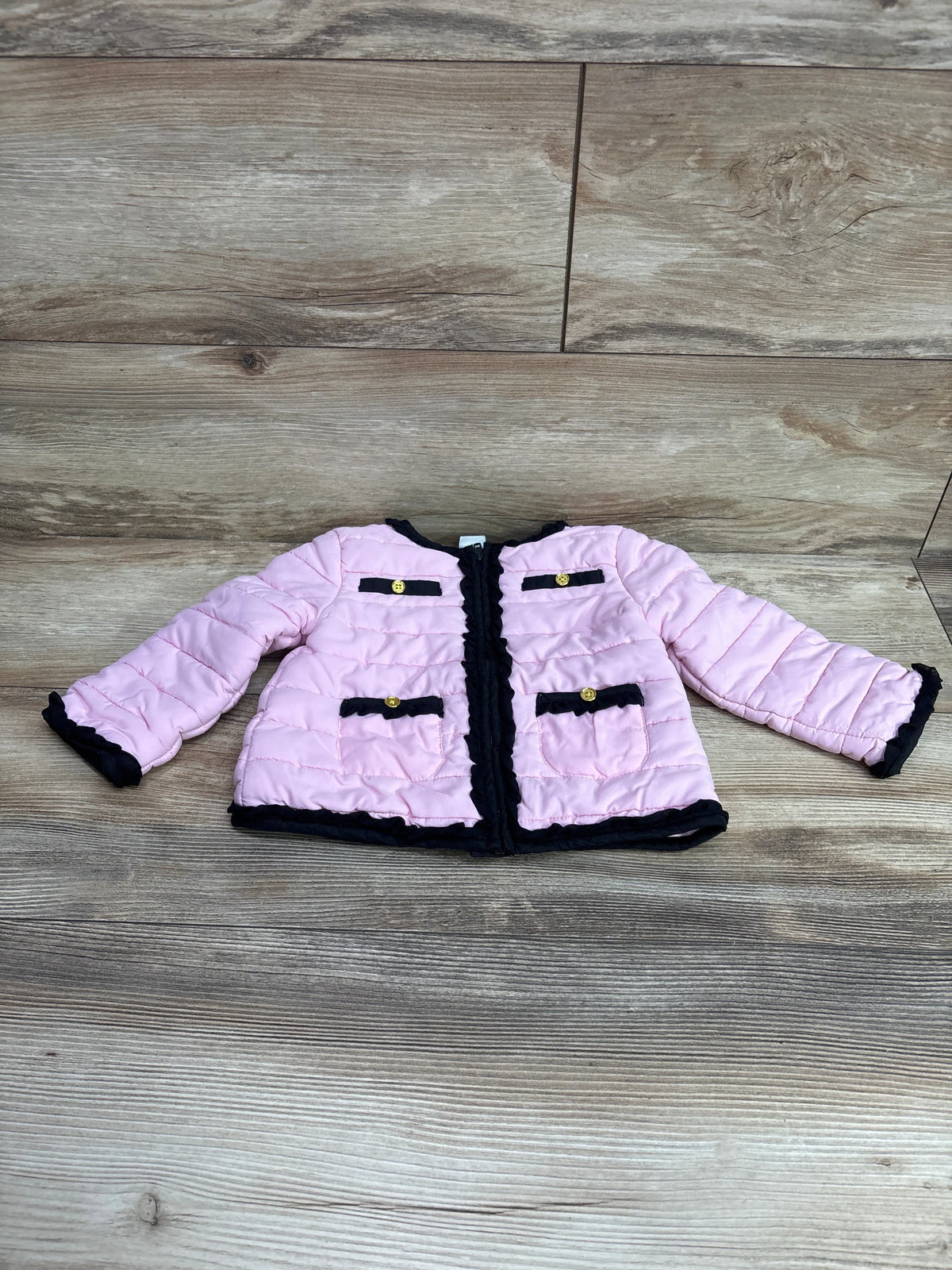 Front view of Little Me pink lightweight puffer jacket showcasing black trim and four pockets on wood flooring