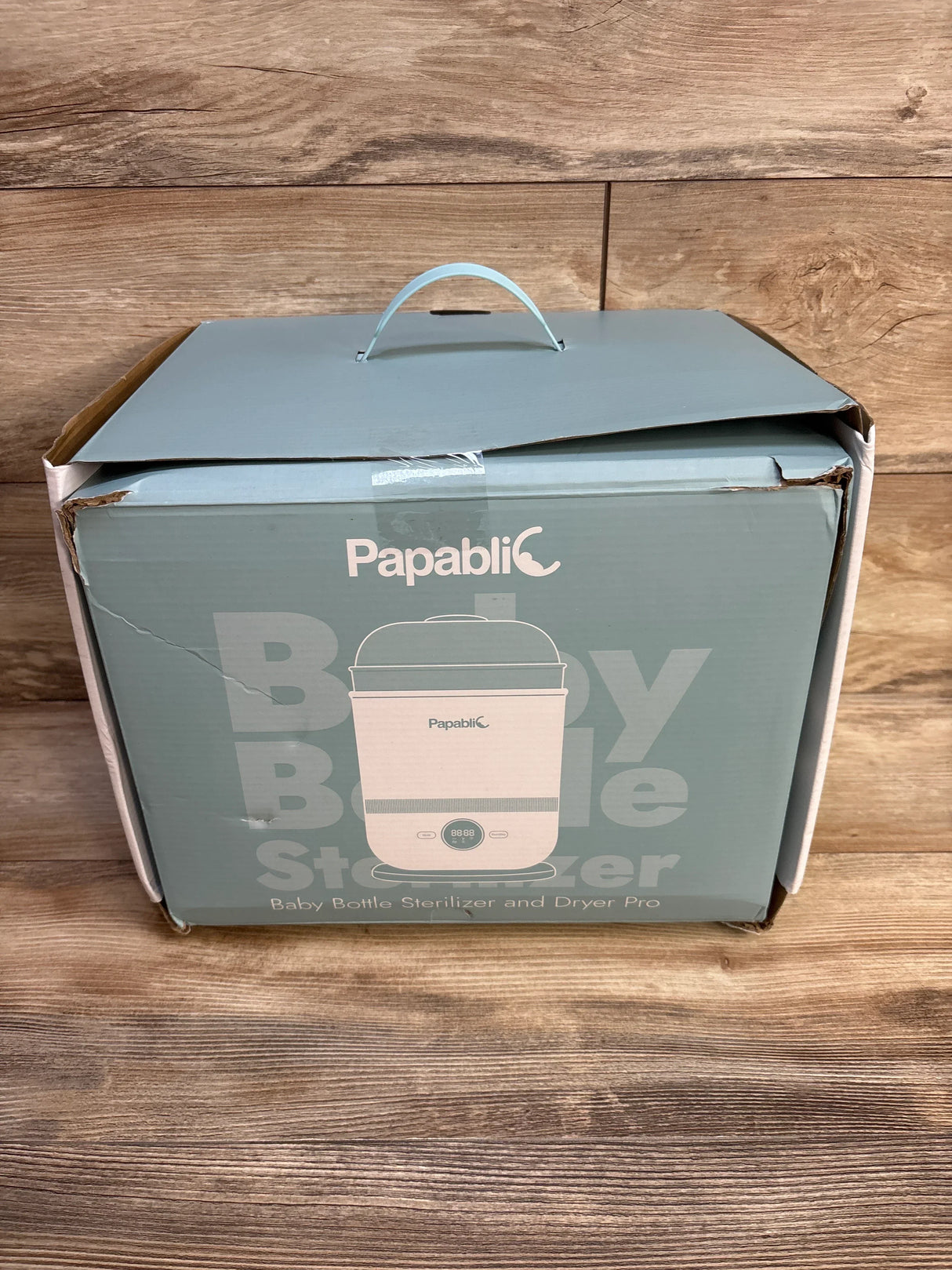 Front view of NEW Papablic Baby Bottle Steam Sterilizer and Dryer Pro in light blue retail box with carry handle on wood plank background