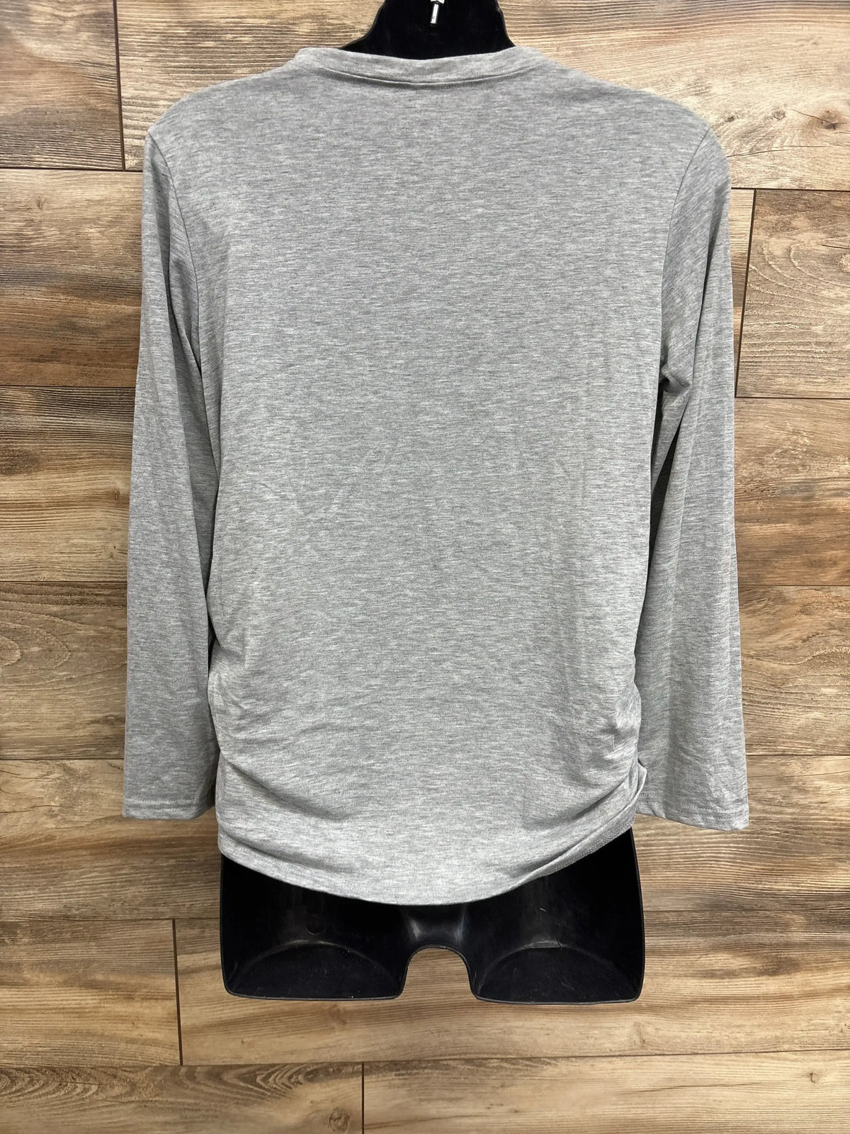 Back view of maternity long-sleeve “Hello Excuse Me Is It May Yet” shirt showing side ruching on gray fabric on mannequin against wood background