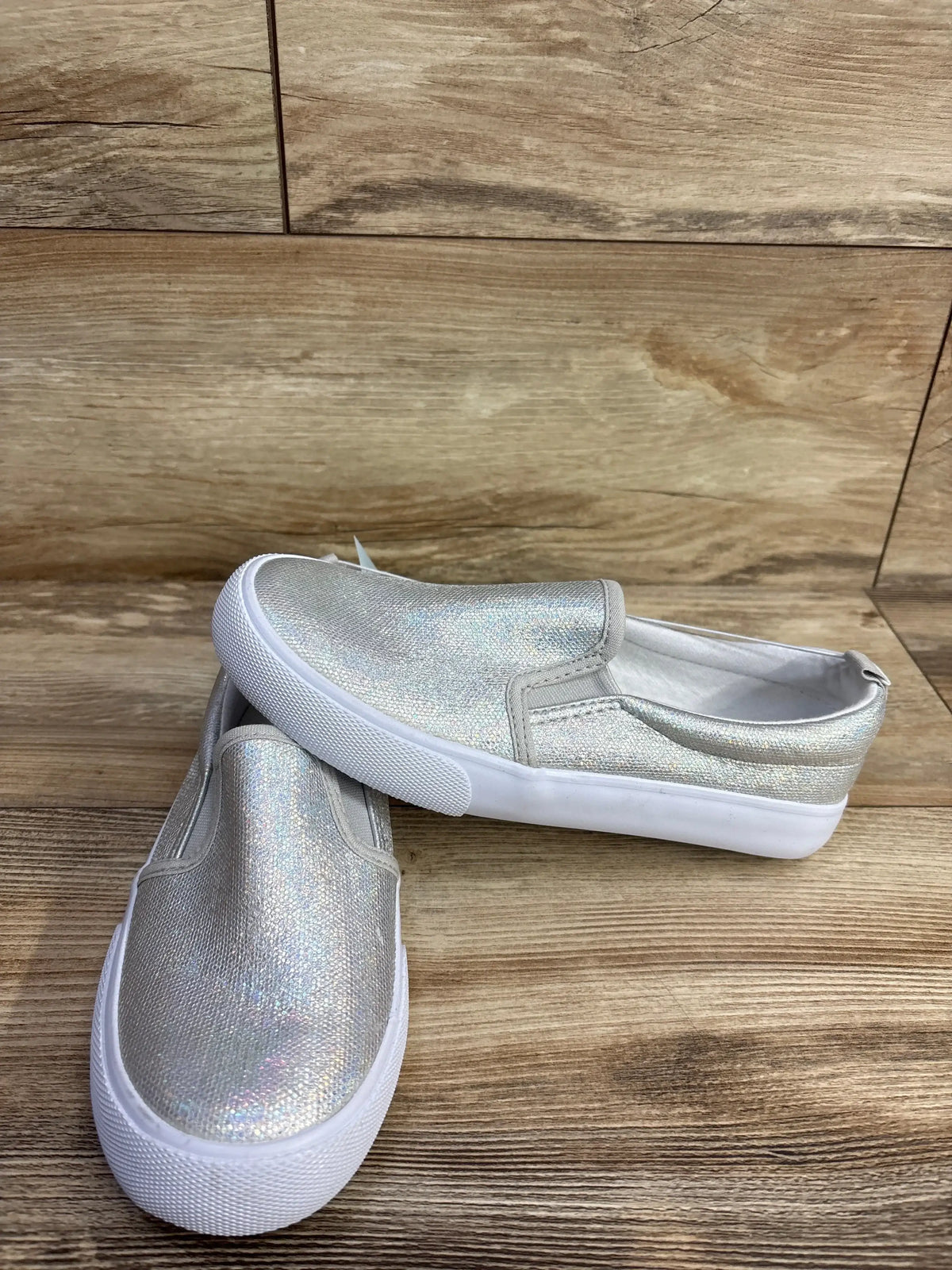 Pair of silver glitter slip-on kids shoes with white soles on wooden background