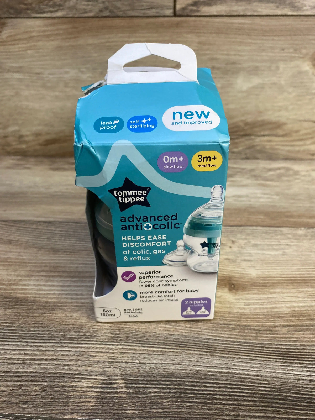 Front view of Tommee Tippee Advanced Anti-Colic 5oz (150ml) in blue packaging with 0m+ and 3m+ labels and two nipples on wood
