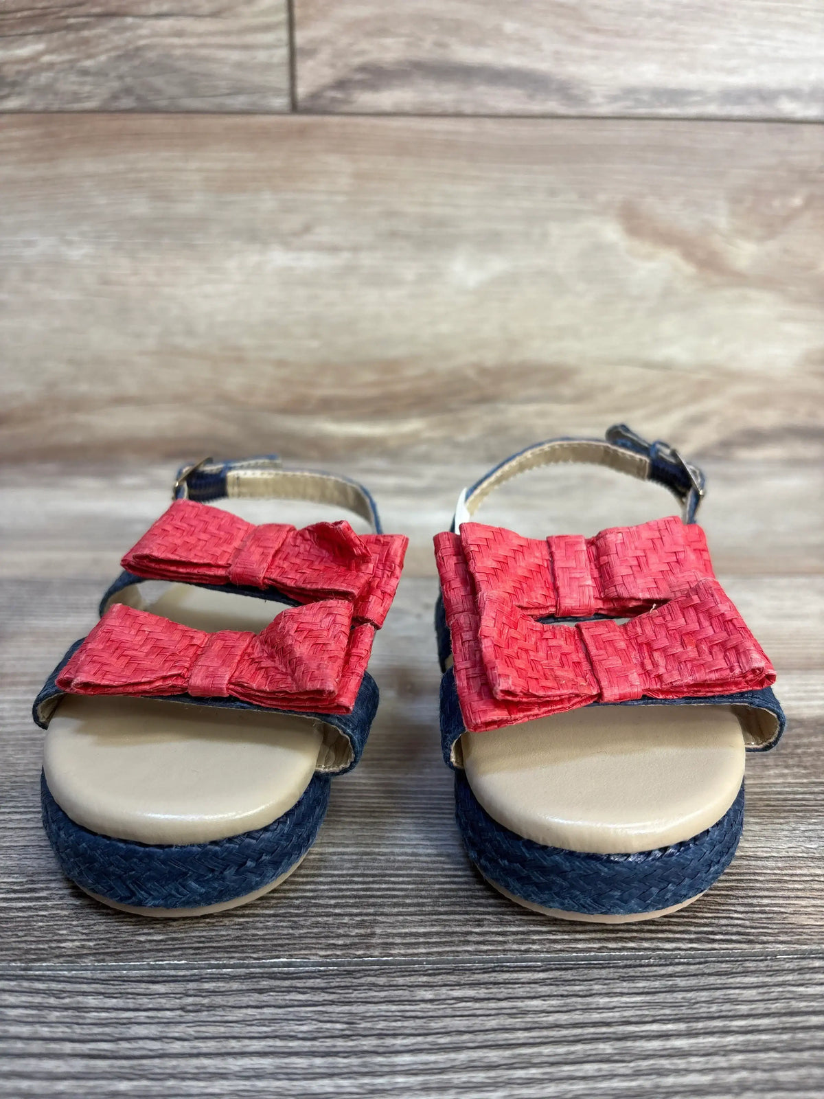 Girls' sandals with navy woven soles and red bow straps on wooden background