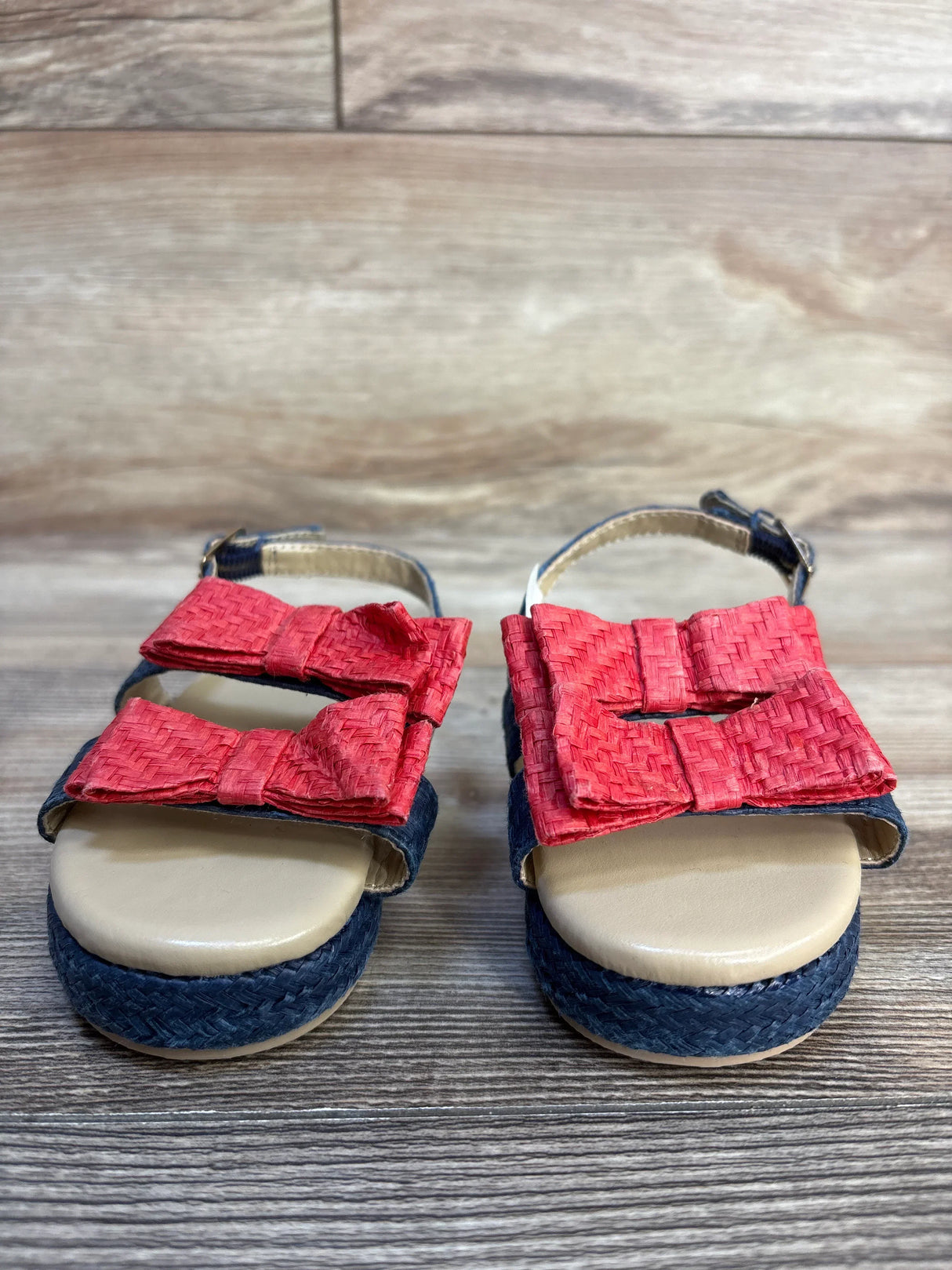 Girls' sandals with navy woven soles and red bow straps on wooden background