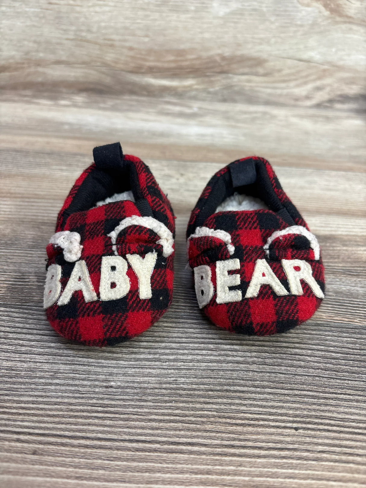 Red and black plaid baby shoes with 'Baby Bear' letters and bear ears on wood background
