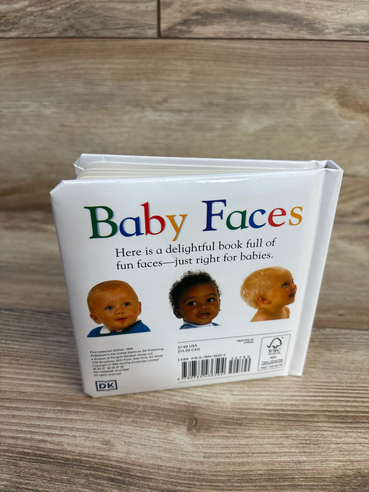 Back cover view of Baby Faces DK board book showcasing three baby portraits and colorful title text on wood plank floor
