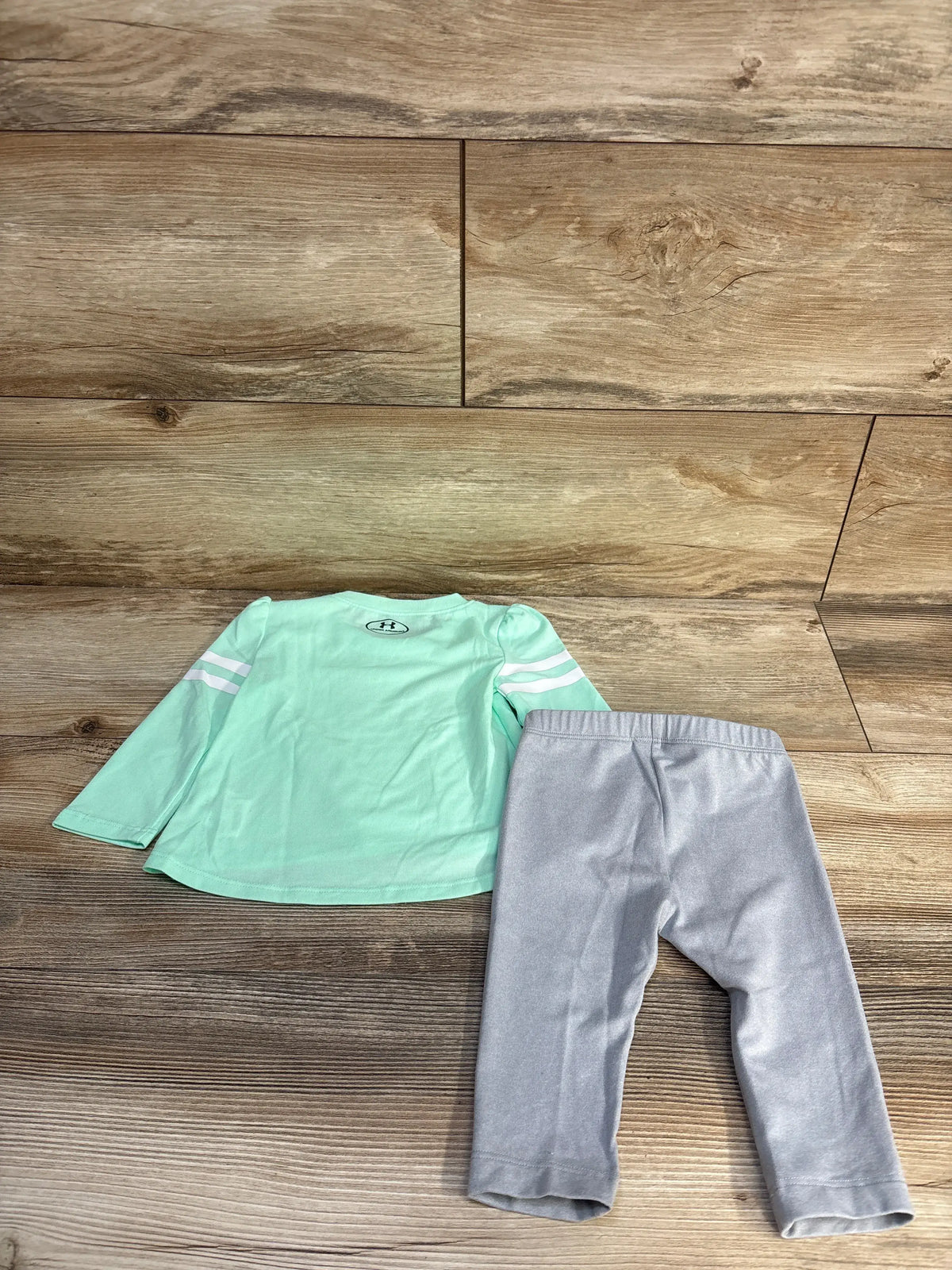 Flat lay of Under Armour teal long sleeve shirt and pants set showing white sleeve stripes on wood background