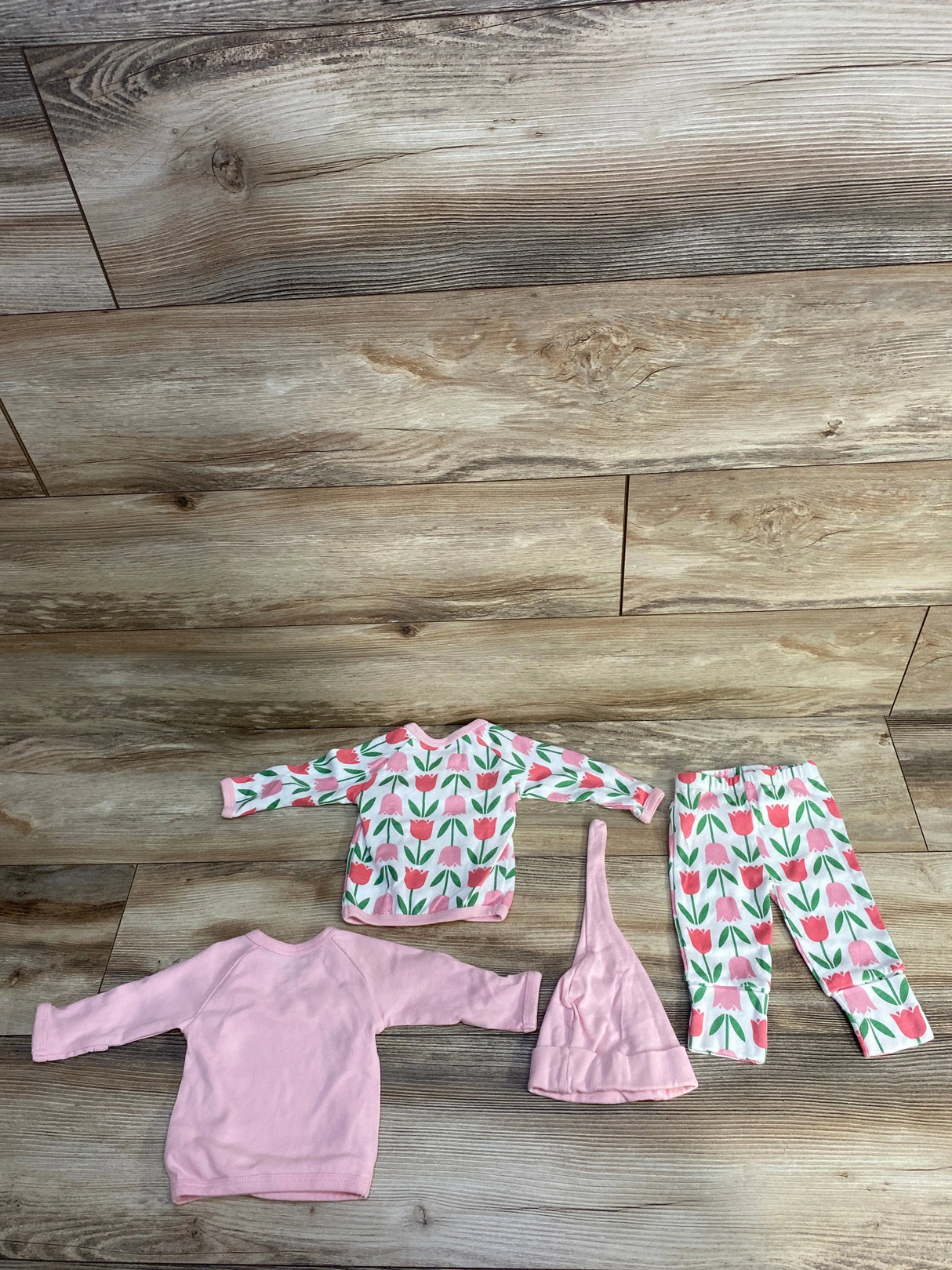 Baby clothes set with pink tulip print top, matching pants, solid pink long-sleeve shirt, and pointed hat on wood floor