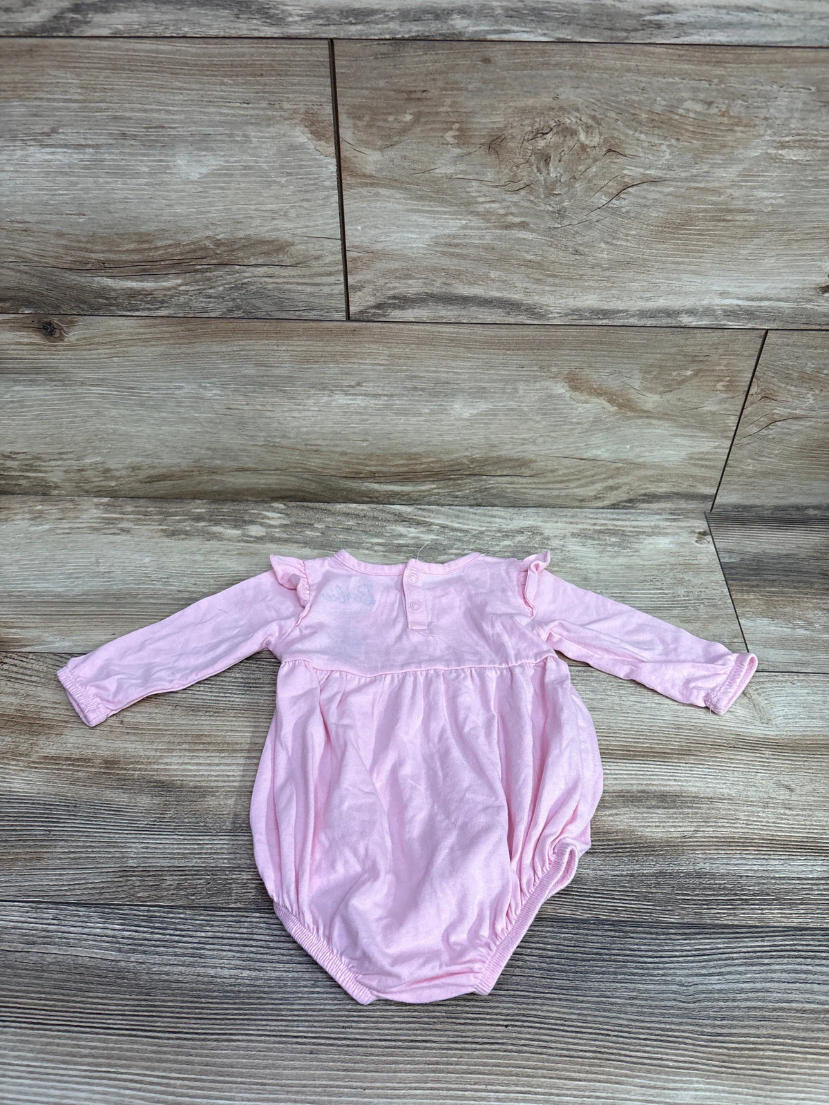 Front view of Barbie pink long sleeve bubble romper, size 3 months, showcasing ruffled shoulders with wood floor background
