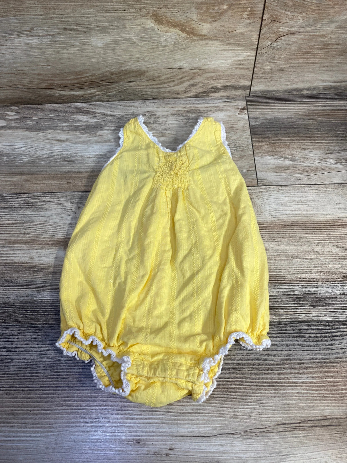 Flat-lay of yellow baby romper (12 months) showing smocked front and white lace trim on wood background
