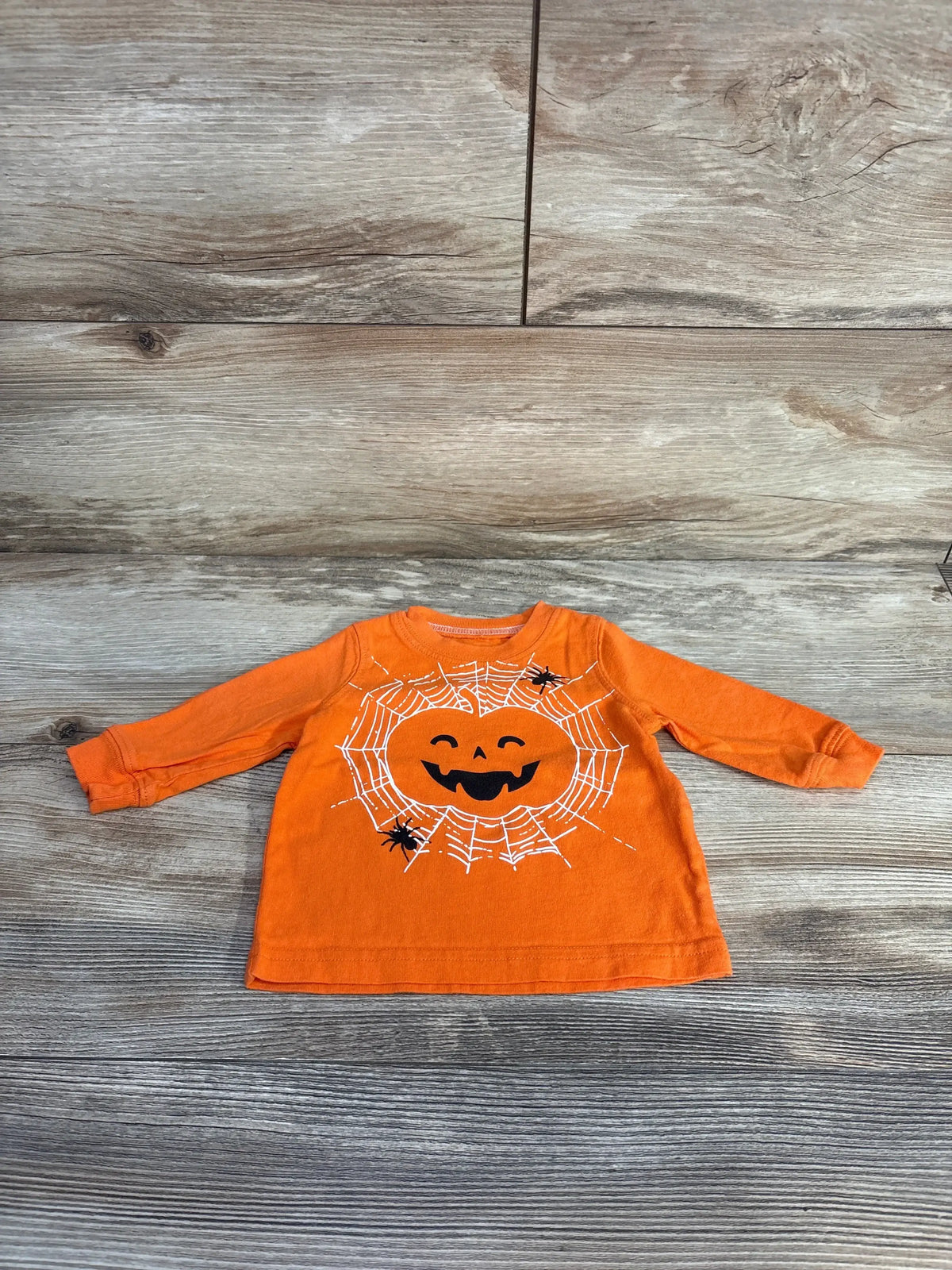 Front view of Carter’s orange Halloween shirt with jack-o-lantern, spiderwebs, and spiders on wood grain
