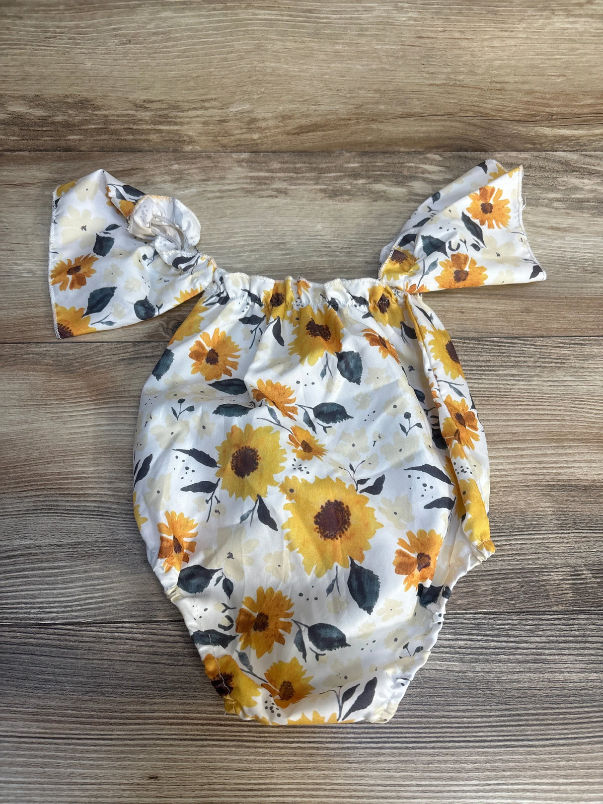 Baby floral romper with yellow sunflowers on wooden background, gently used kids clothing