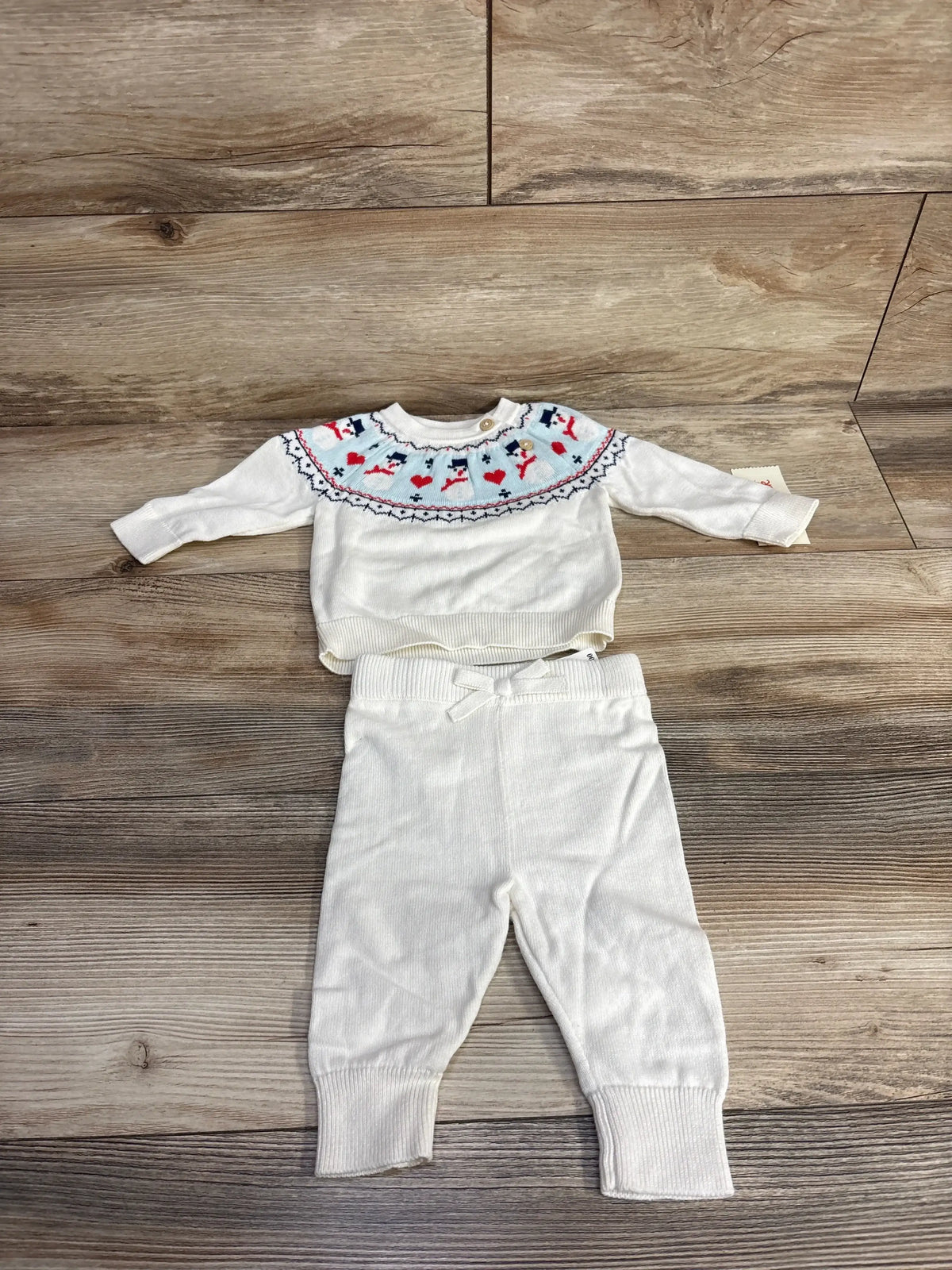 Top-down view of Cat & Jack newborn white knit sweater and pants set showcasing snowman Fair Isle yoke, ribbed cuffs, and drawstring waist on wood floor