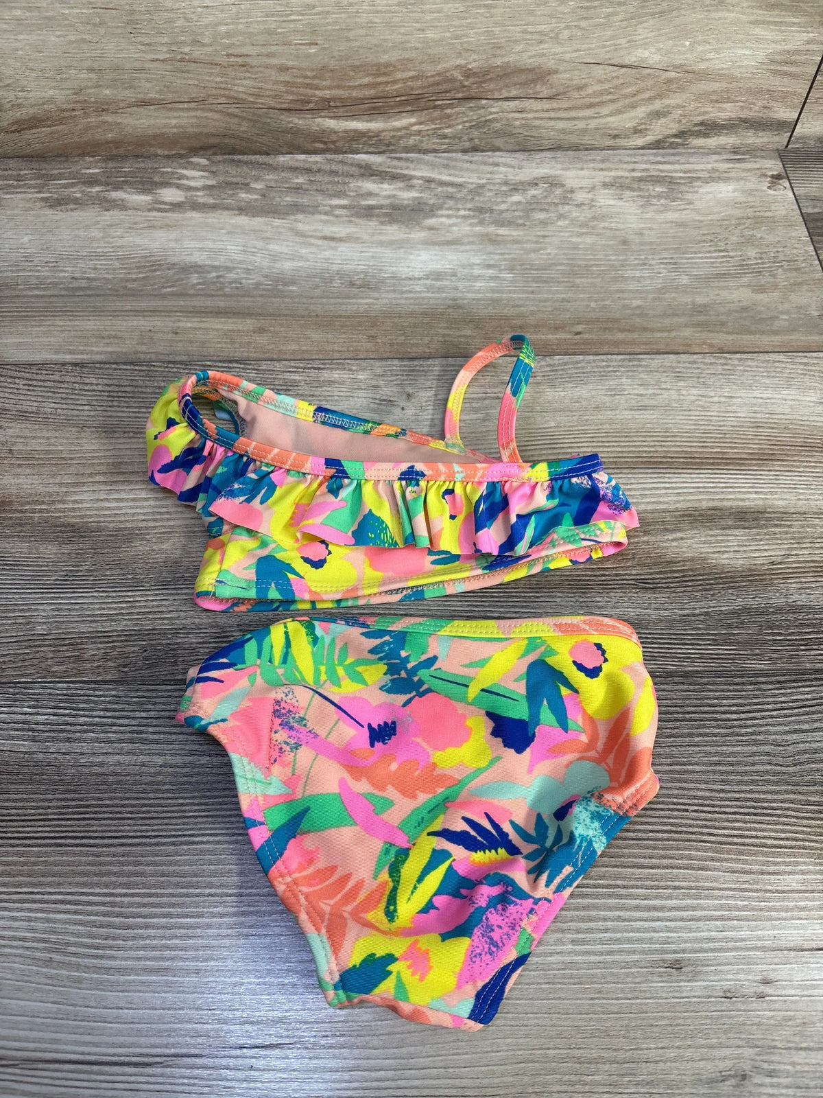 Top-down view of Cat & Jack two-piece swimsuit set in peach showcasing a ruffled top and colorful floral print on a wood floor