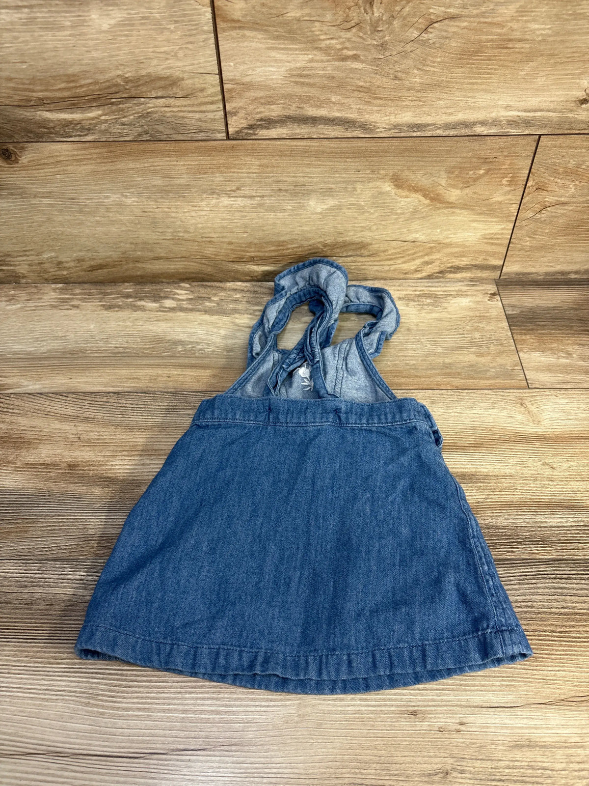 Front view of Old Navy embroidered denim skirtall showcasing blue denim, bib straps, and embroidered detail on a wood-look floor