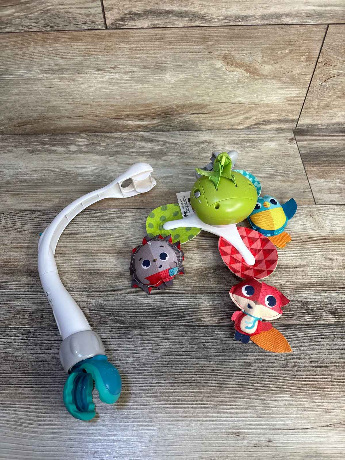 Top view of Tiny Love 3-in-1 Take Along Mobile showcasing colorful hanging toys and white attachment arm on a wood floor