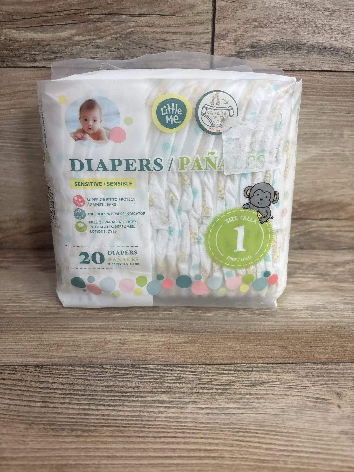 Front view of Little Me size 1 diaper pack showing Sensitive label and 20-count quantity on a wood floor background