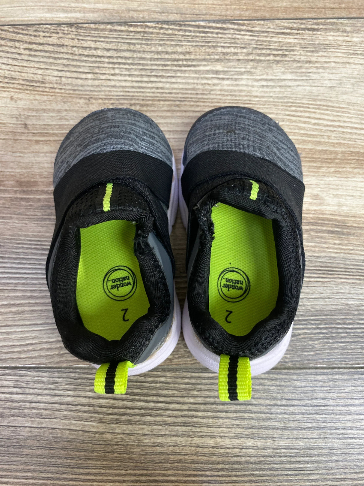 Toddler size 2 slip-on sneakers, gray and black with neon green accents, on wood floor