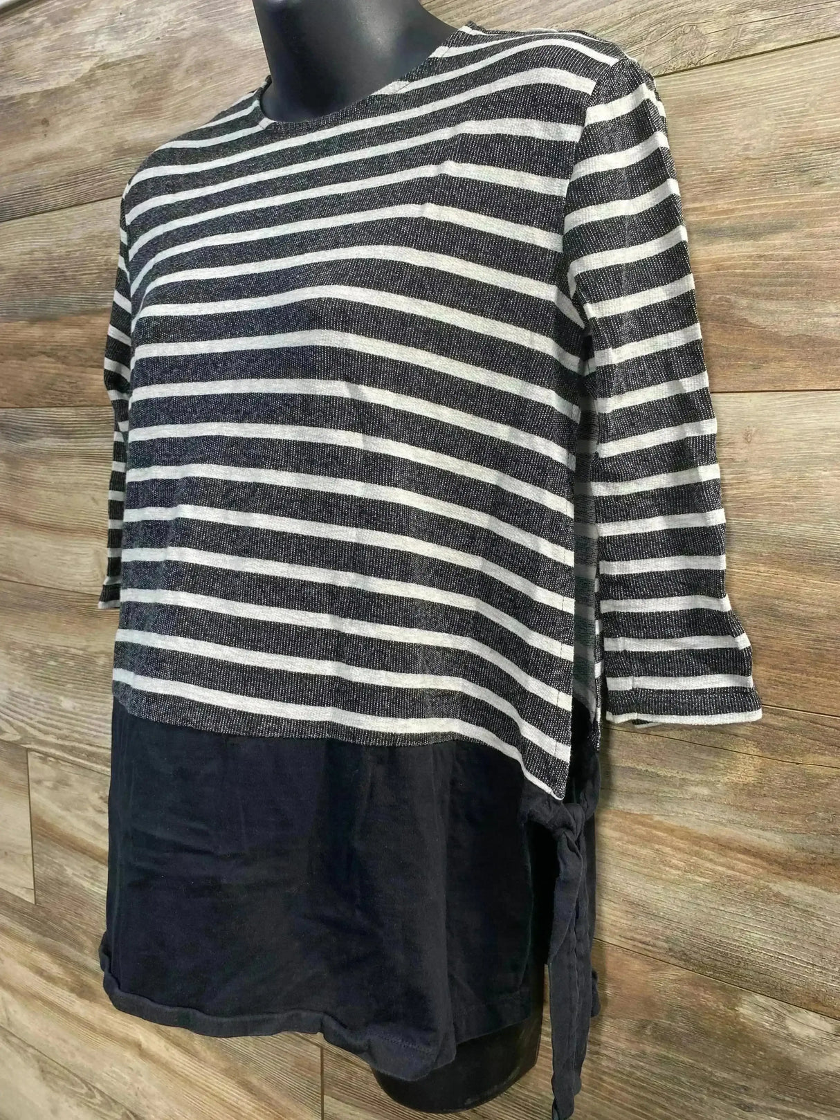 Angled front view of ASOS maternity top with black-and-white stripes, solid black lower panel and side tie on wood background