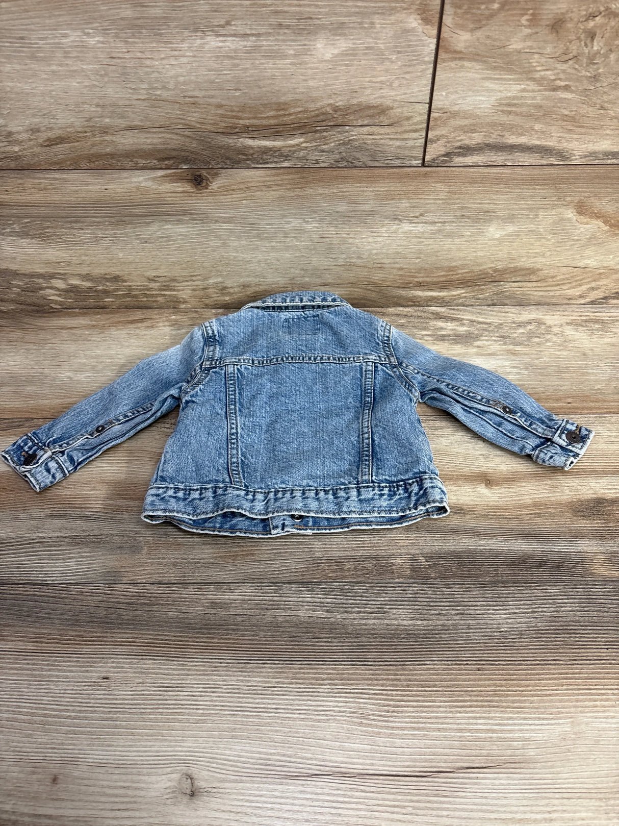 Back view of a gently used light wash denim jacket for toddlers laid flat on wooden floor
