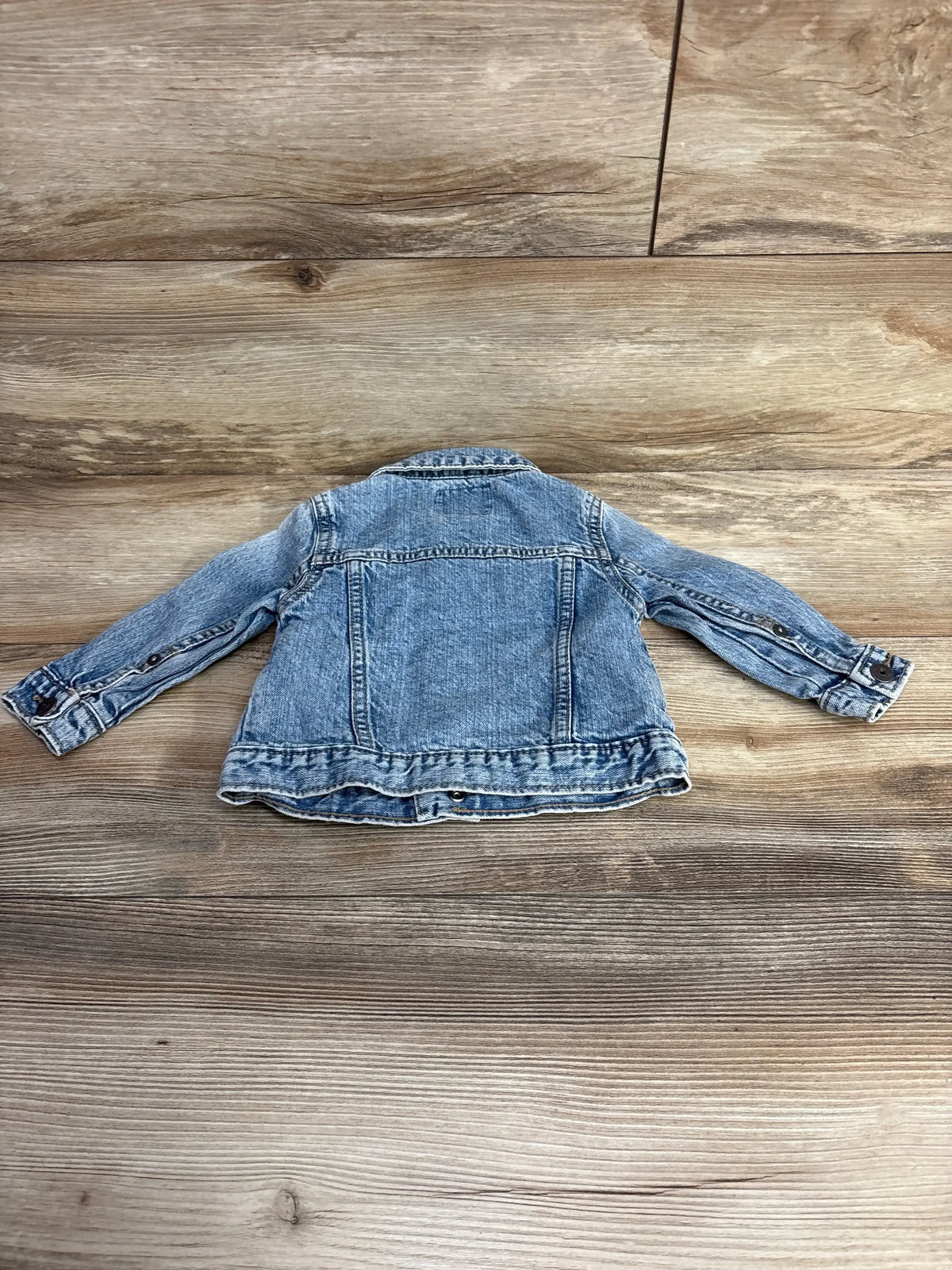 Back view of a gently used light wash denim jacket for toddlers laid flat on wooden floor