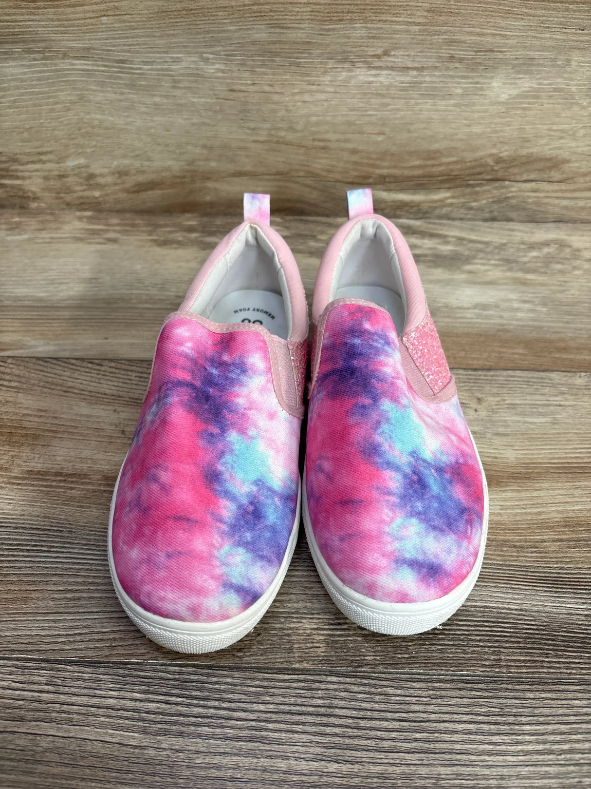 Pair of pink, purple, and blue tie-dye slip-on kids shoes with white soles on wood floor