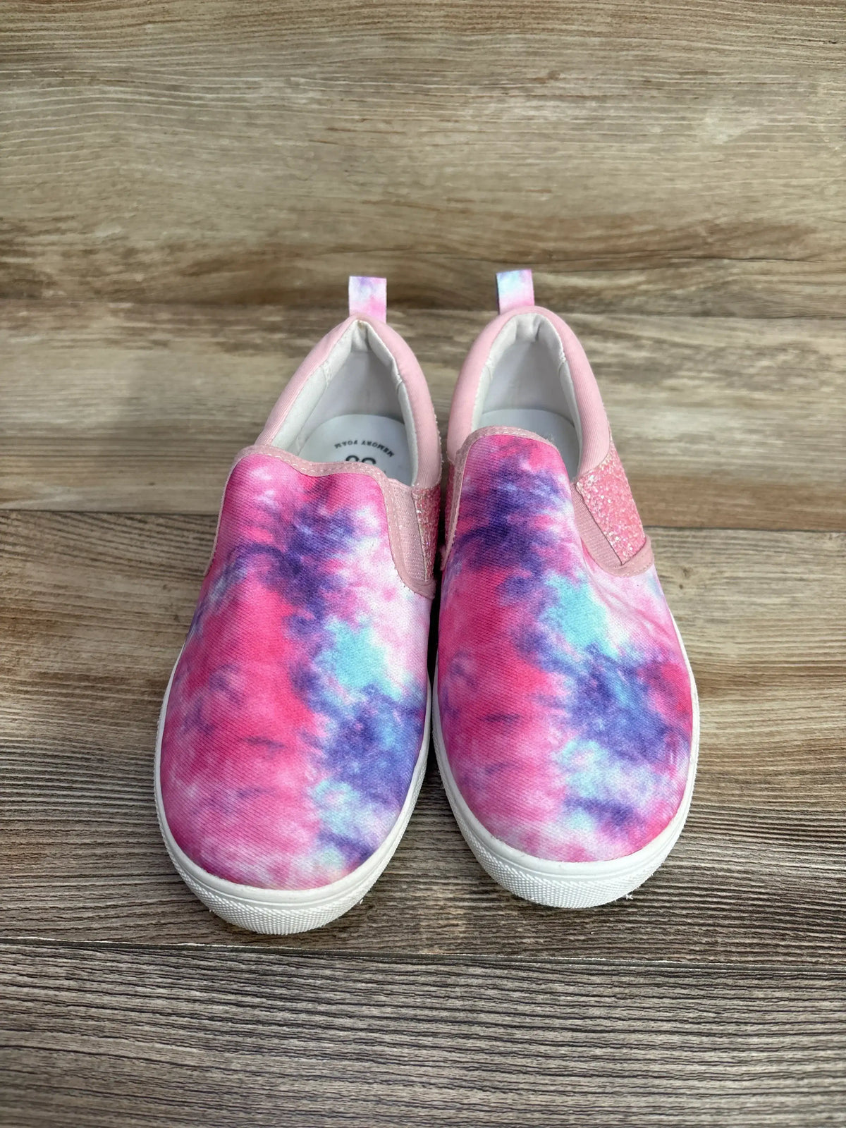 Pair of pink, purple, and blue tie-dye slip-on kids shoes with white soles on wood floor