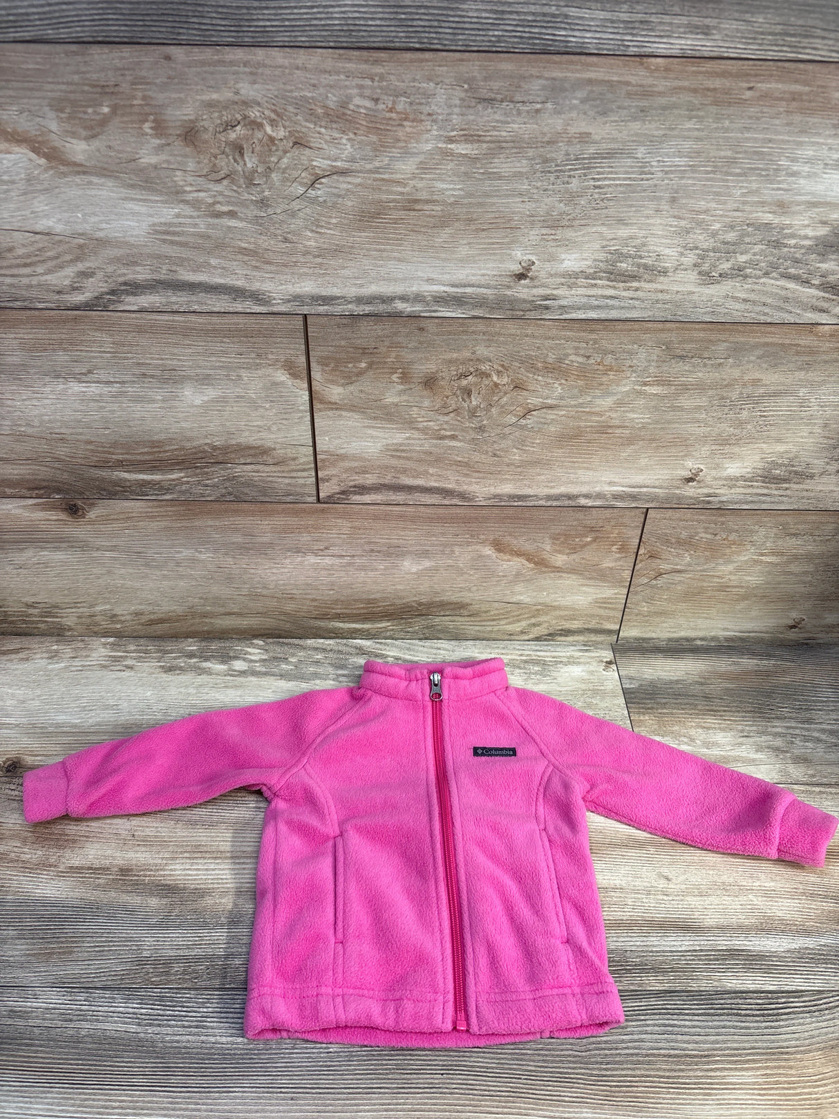 Front view of Columbia fleece full-zip jacket size 12-18 months in bright pink showing zipper, side pockets and logo on wood background