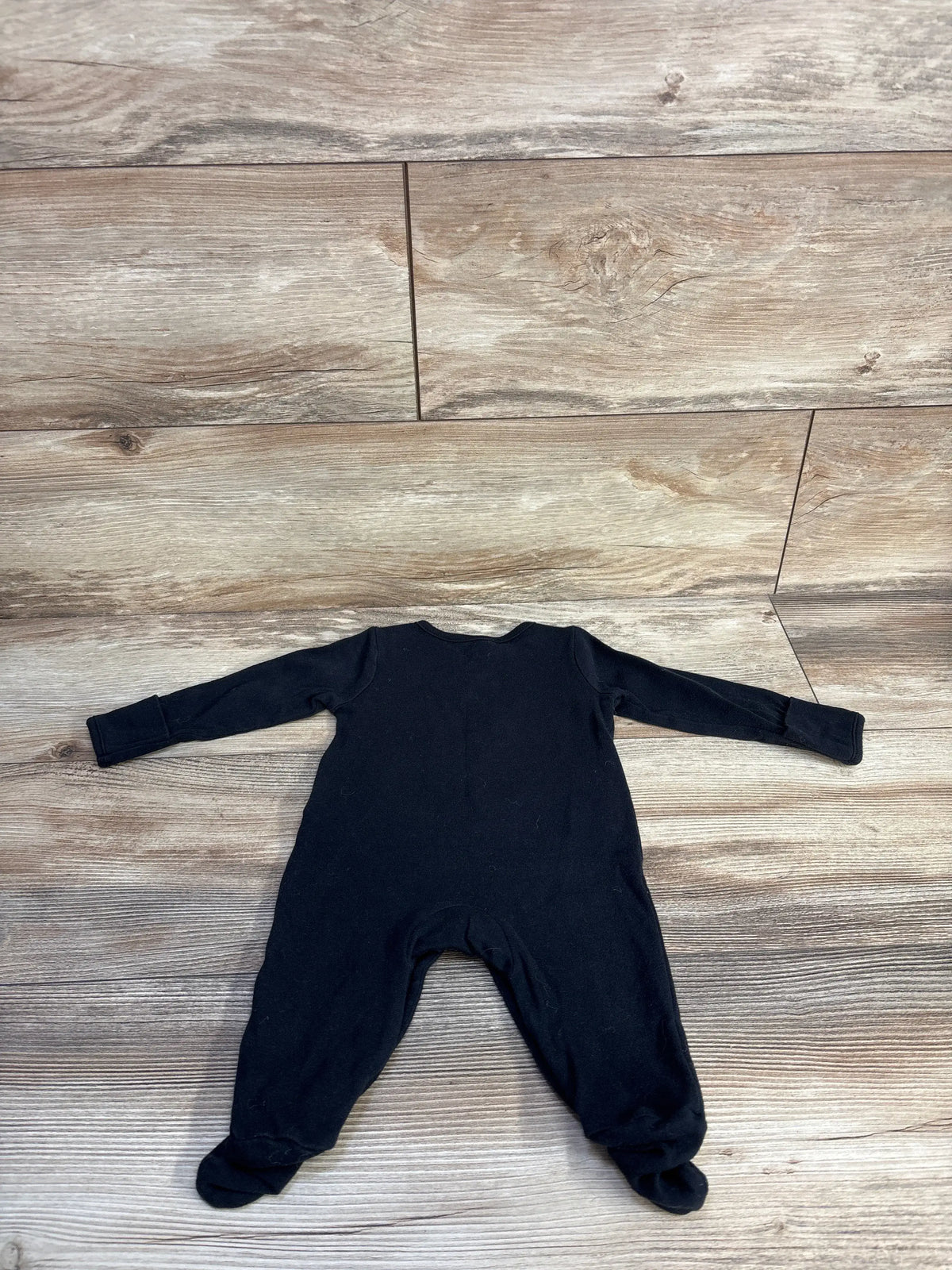 Top view of black Just One You skeleton footed coverall with long sleeves and covered feet on a wood-look floor