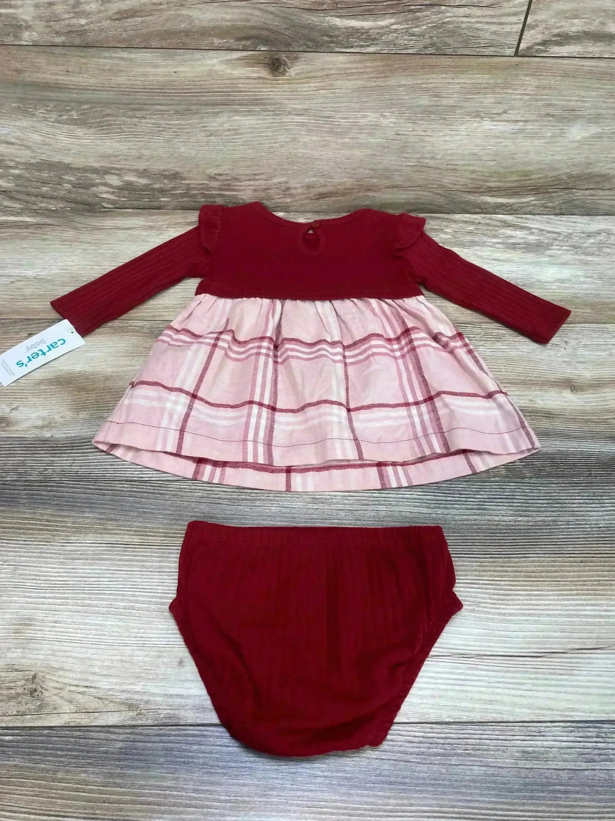 Flat lay of Carter’s red ribbed long-sleeve baby dress with pink plaid skirt and matching red bloomers on wood background