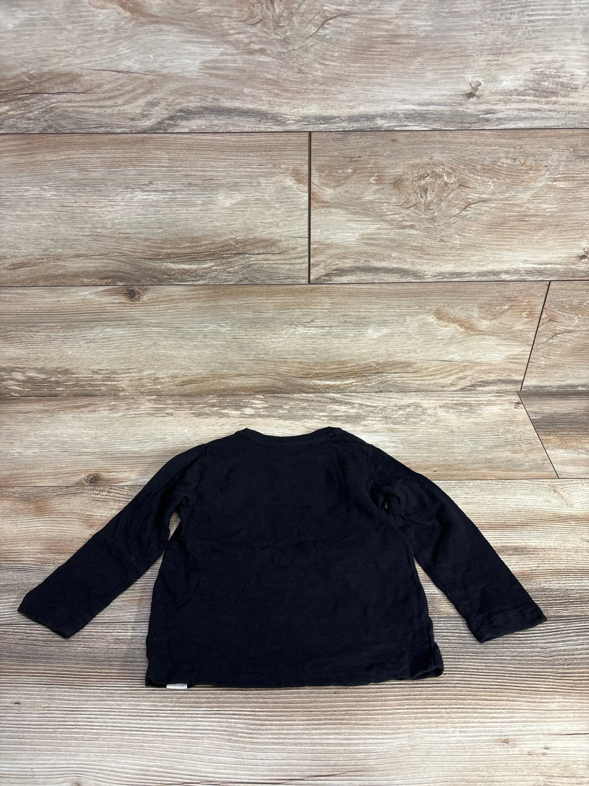 Black long sleeve kids shirt laid flat on wood floor, resale clothing for children
