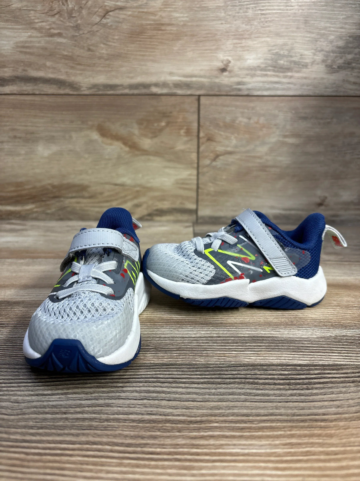 Gray and blue kids' athletic sneakers with velcro straps on wood floor