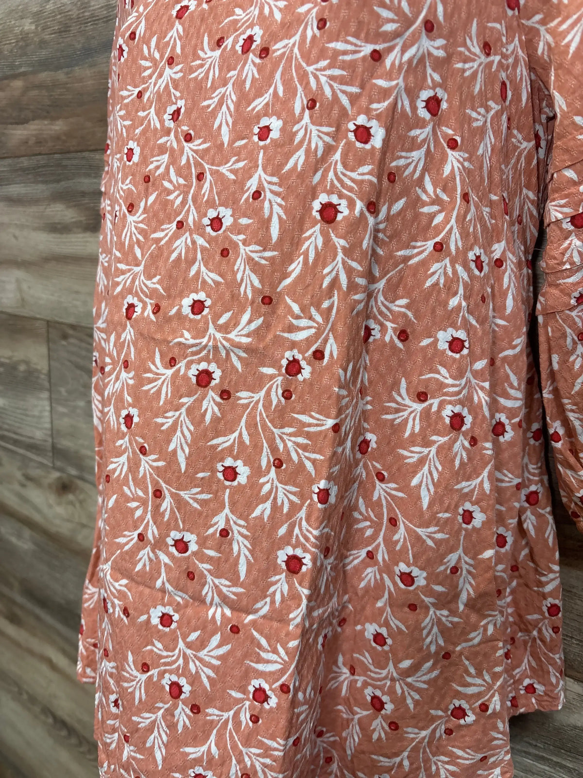 Close-up of Isabel maternity floral blouse showing orange fabric with white embroidered leaves and red centers on wood background