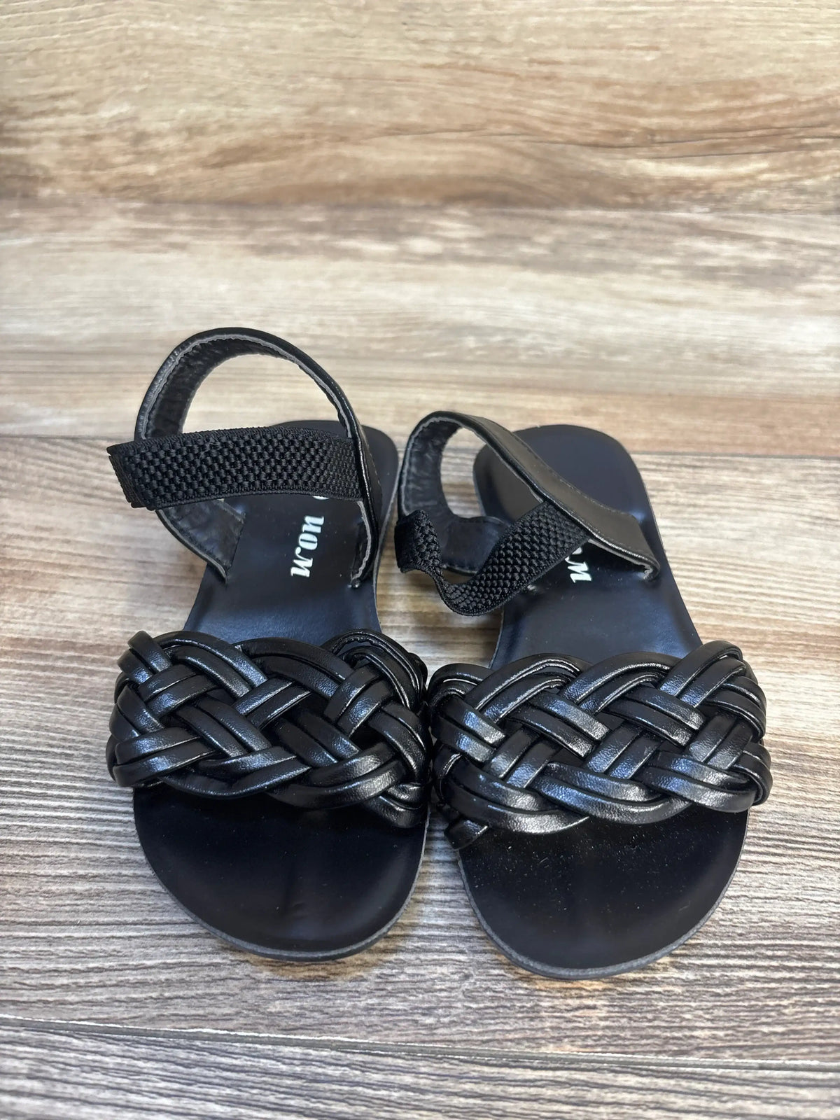 Black toddler sandals with braided straps and Velcro closures on wood background