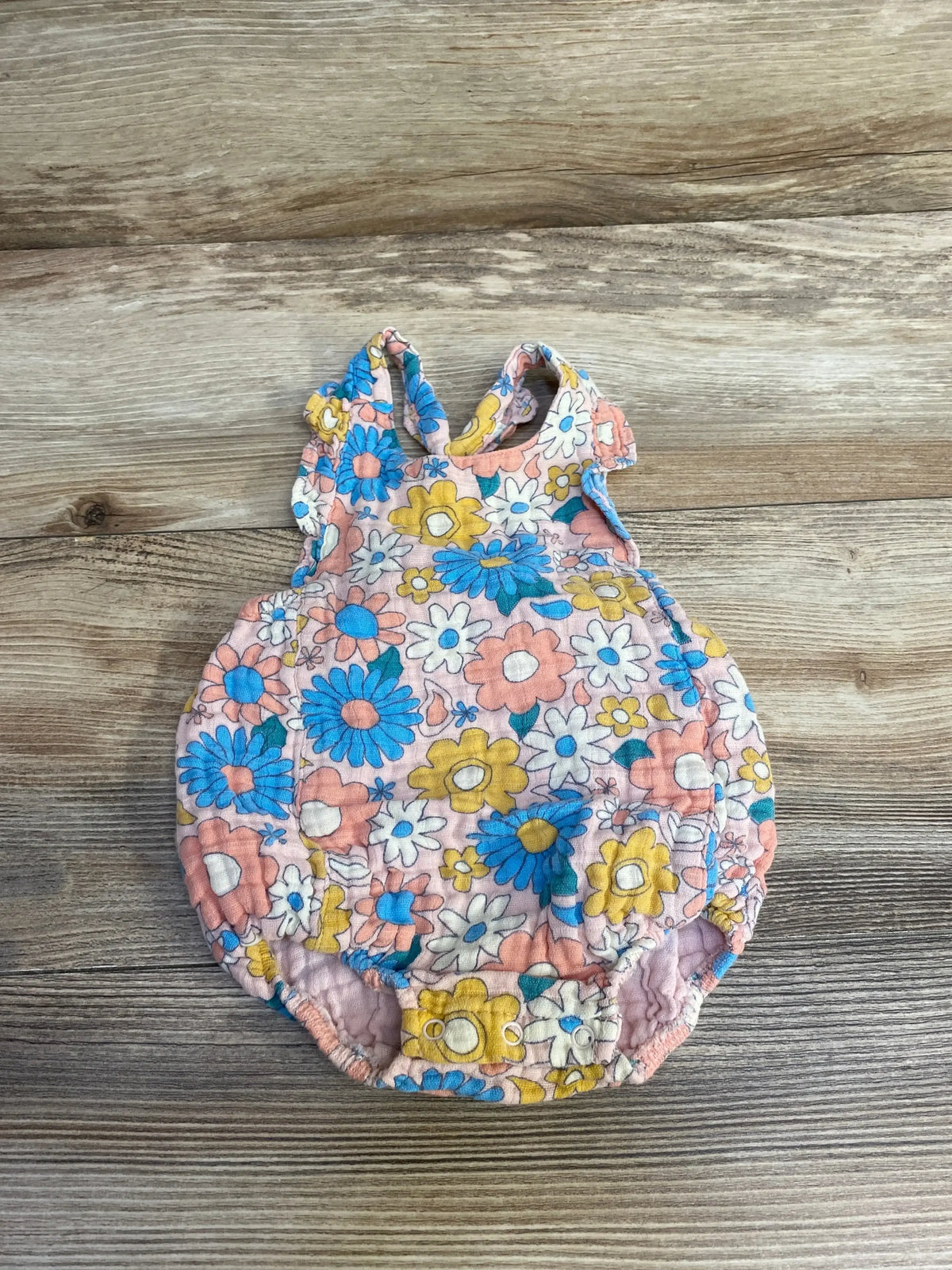 Flat lay of Angel Dear Groovy Daisy romper showcasing pink daisy print, sleeveless bubble with snap crotch on wood background