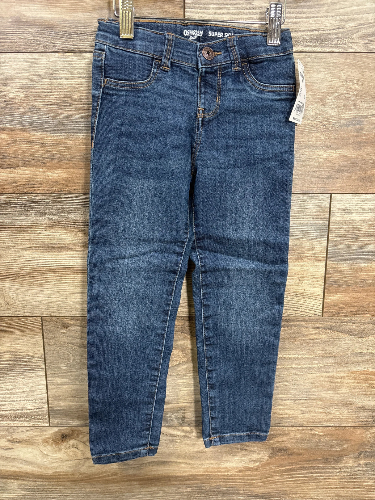 Dark wash kids skinny jeans with front pockets displayed on wooden background