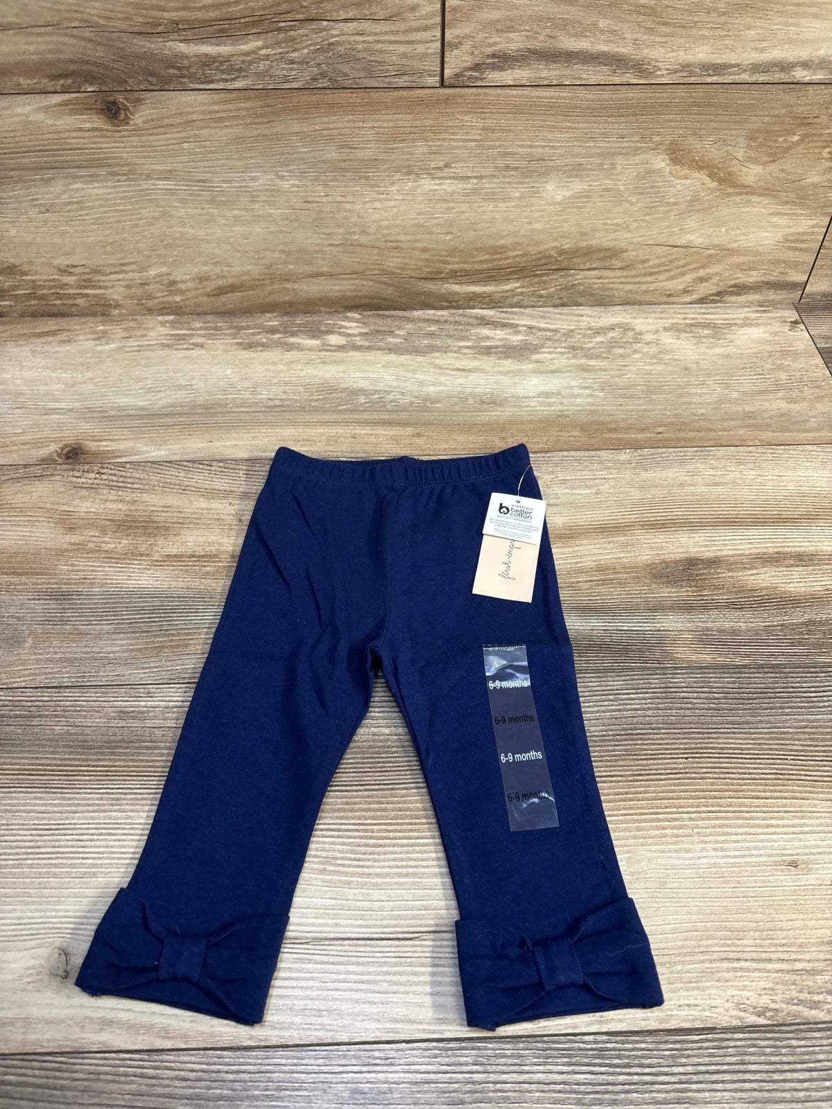 Front view of navy blue baby leggings (6-9 months) showcasing bow-trim cuffs and elastic waist with wood floor background