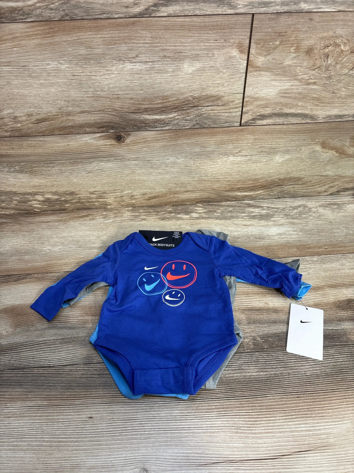 Blue Nike baby bodysuit with smiley faces, long sleeves, on wooden background