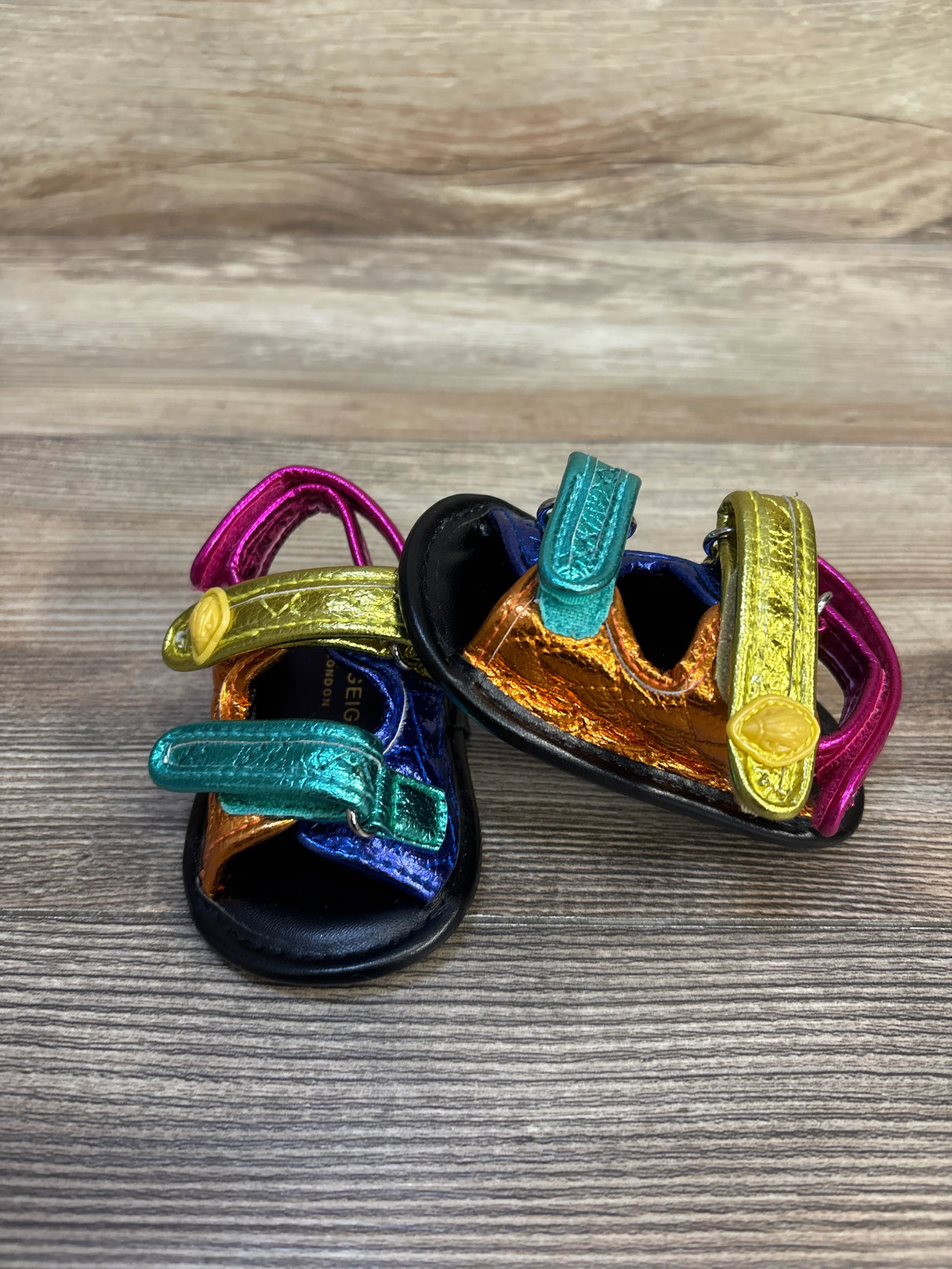 Front view of Kurt Geiger Orson metallic leather sandals size 2C showcasing multicolor straps with Velcro on wood background