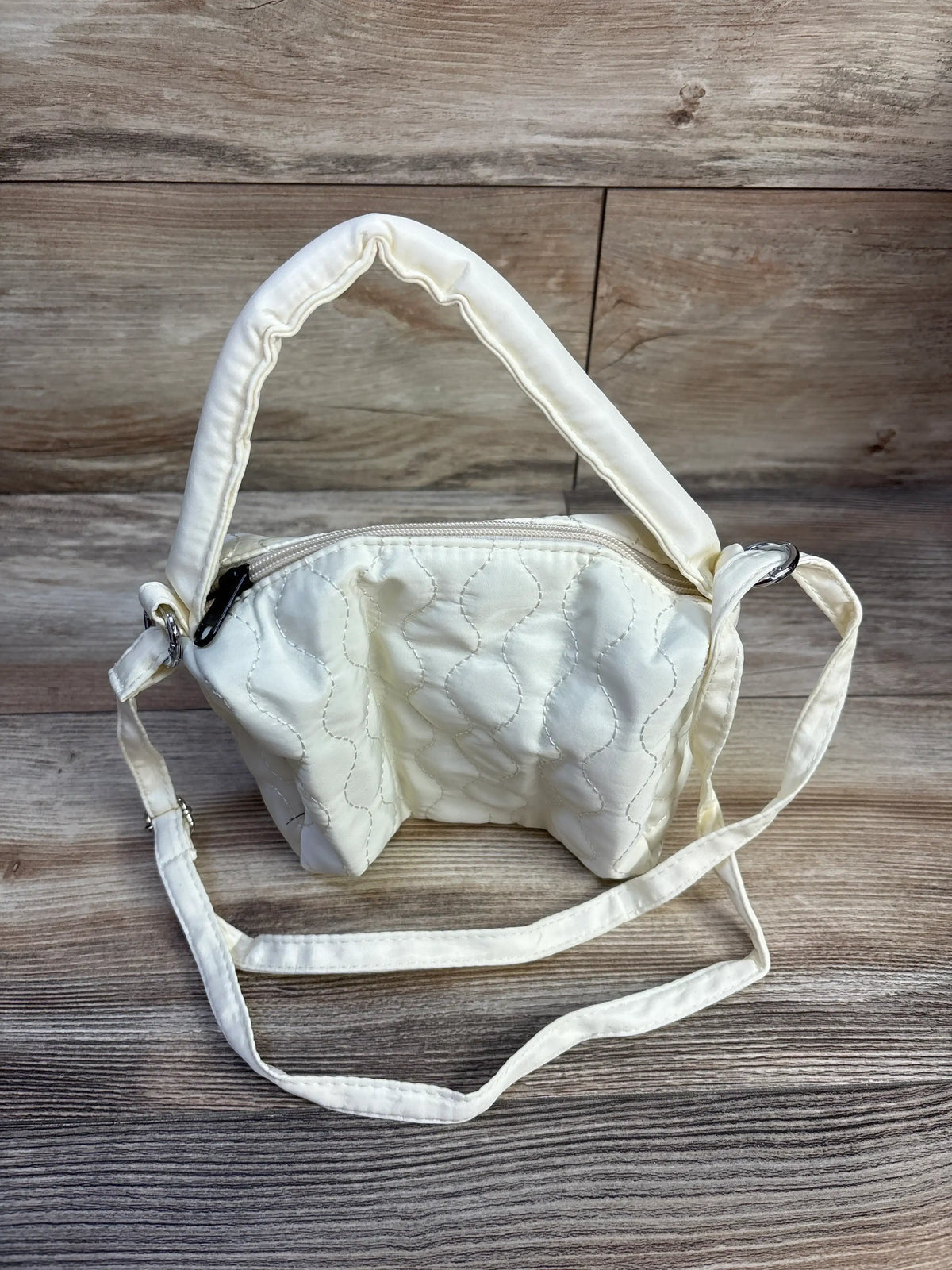 Front view of Ycstudio mini crossbody quilted bag in ivory with padded quilting and long strap on wood-grain background