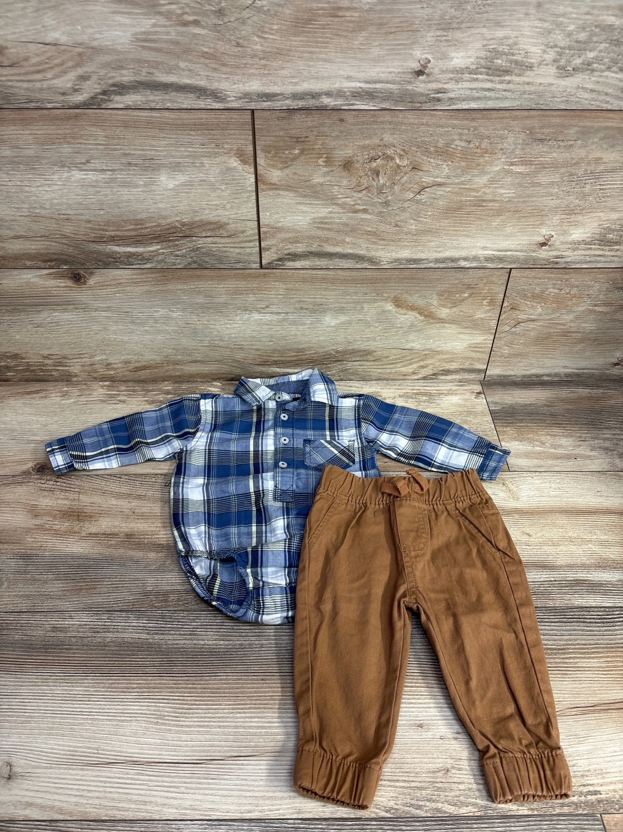 Children's outfit with blue plaid button-up shirt and brown elastic waist pants on wood floor