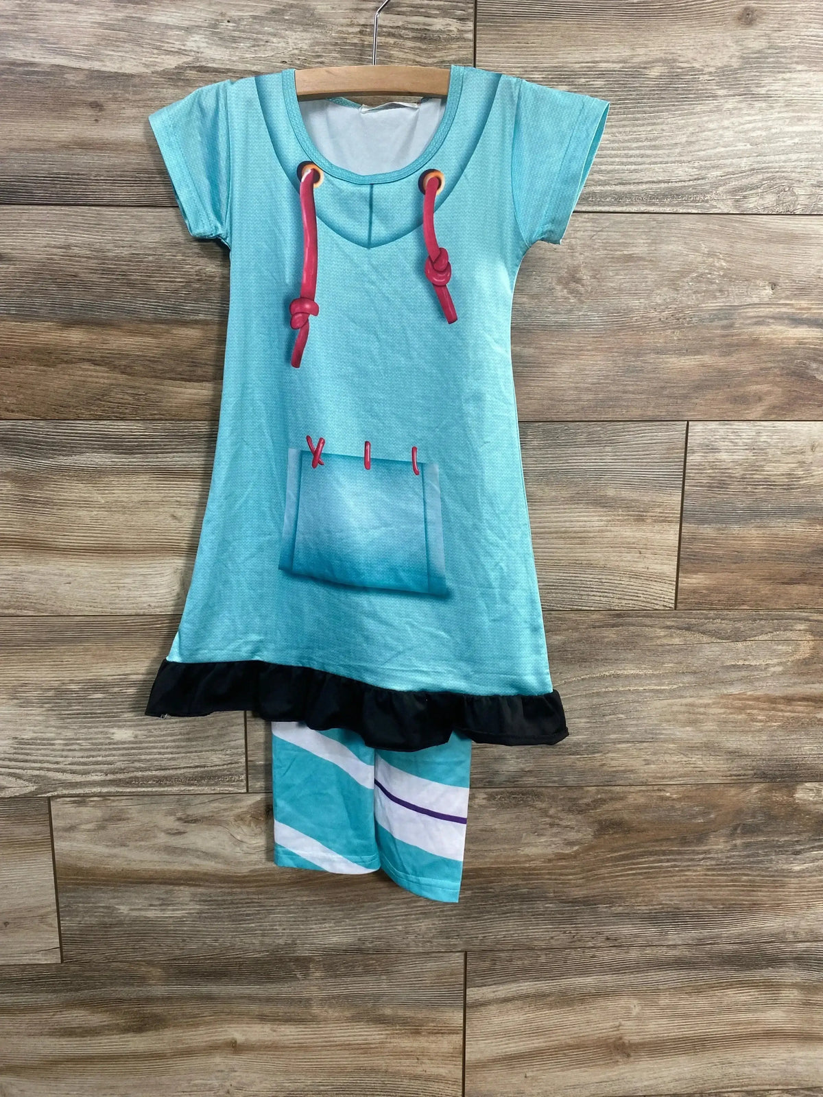 Front view of Vanellope costume showcasing a turquoise dress with red drawstrings, front pocket, black ruffled hem, and striped leggings