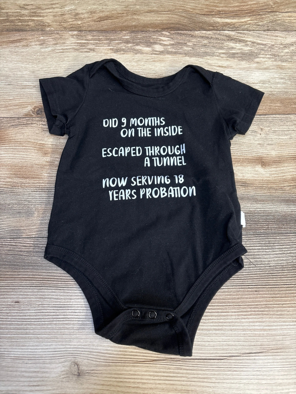 Top down black 18m onesie with white text Did 9 months on the inside Escaped through a tunnel Now serving 18 years probation