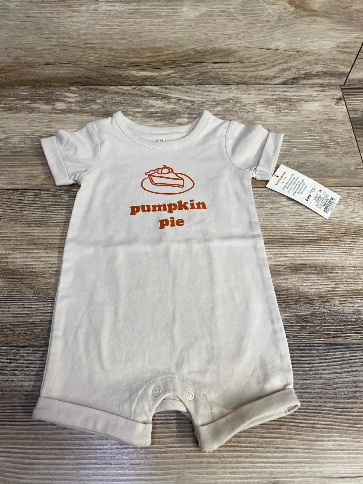 White baby onesie with orange 'pumpkin pie' graphic and slice illustration, size 0-3M, on wood floor