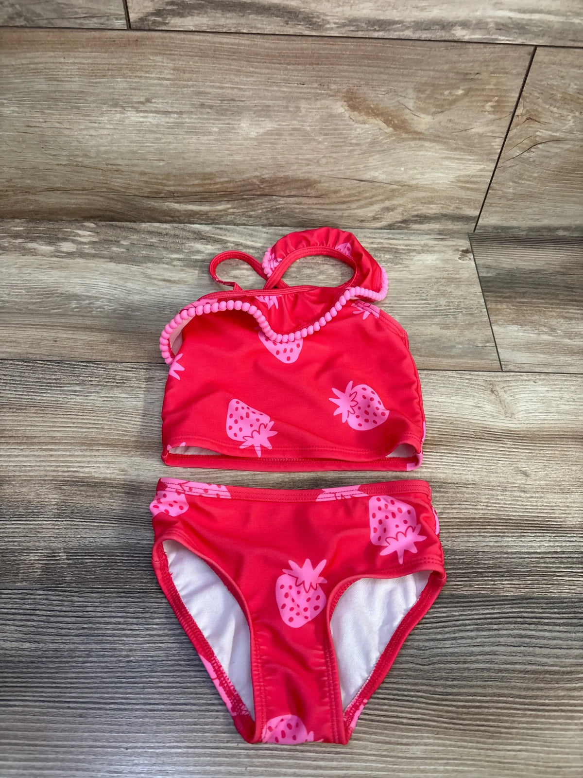Flat lay of Cat & Jack two-piece red strawberry swimsuit, size 12 months, showcasing strawberry print and ruffle trim with wood-look background